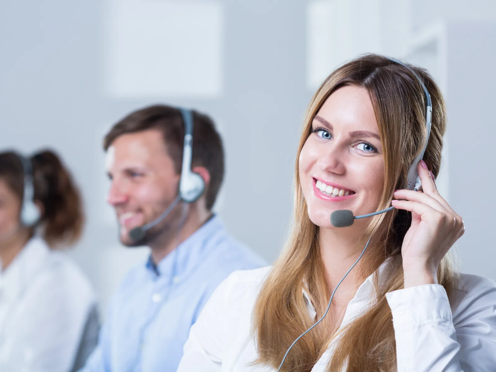 Smiling customer service representatives wearing headsets in a bright office environment helping clients.