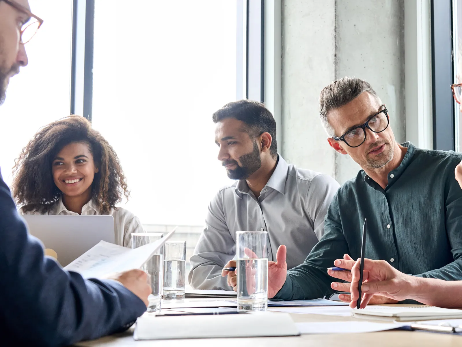 Diverse team engaged in a business meeting around a table with documents and glasses of water.