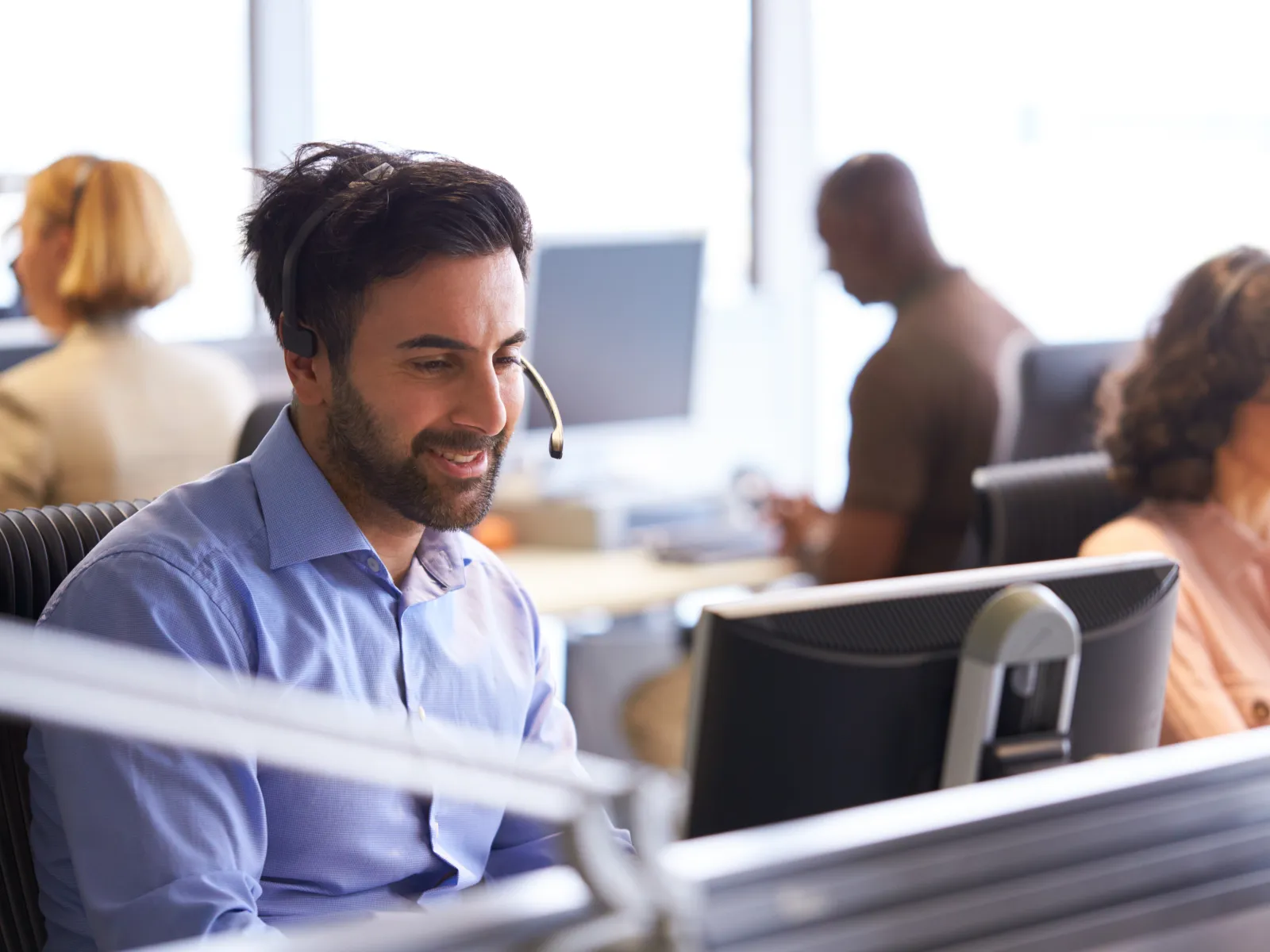 Professionals working in a call center, using headsets and computers, focused on their tasks.