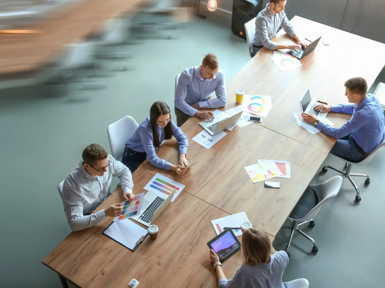 Aerial view of a diverse team collaborating in a modern office space with laptops and color charts.