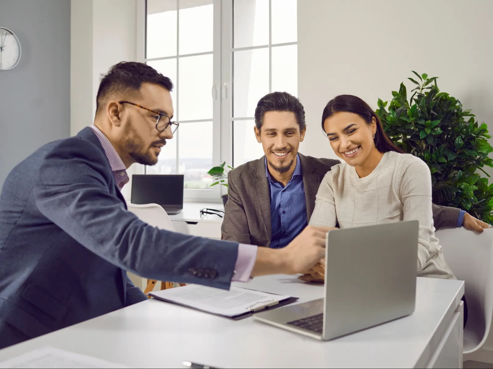 Three professionals collaborating on a laptop in a modern office with large windows and natural light