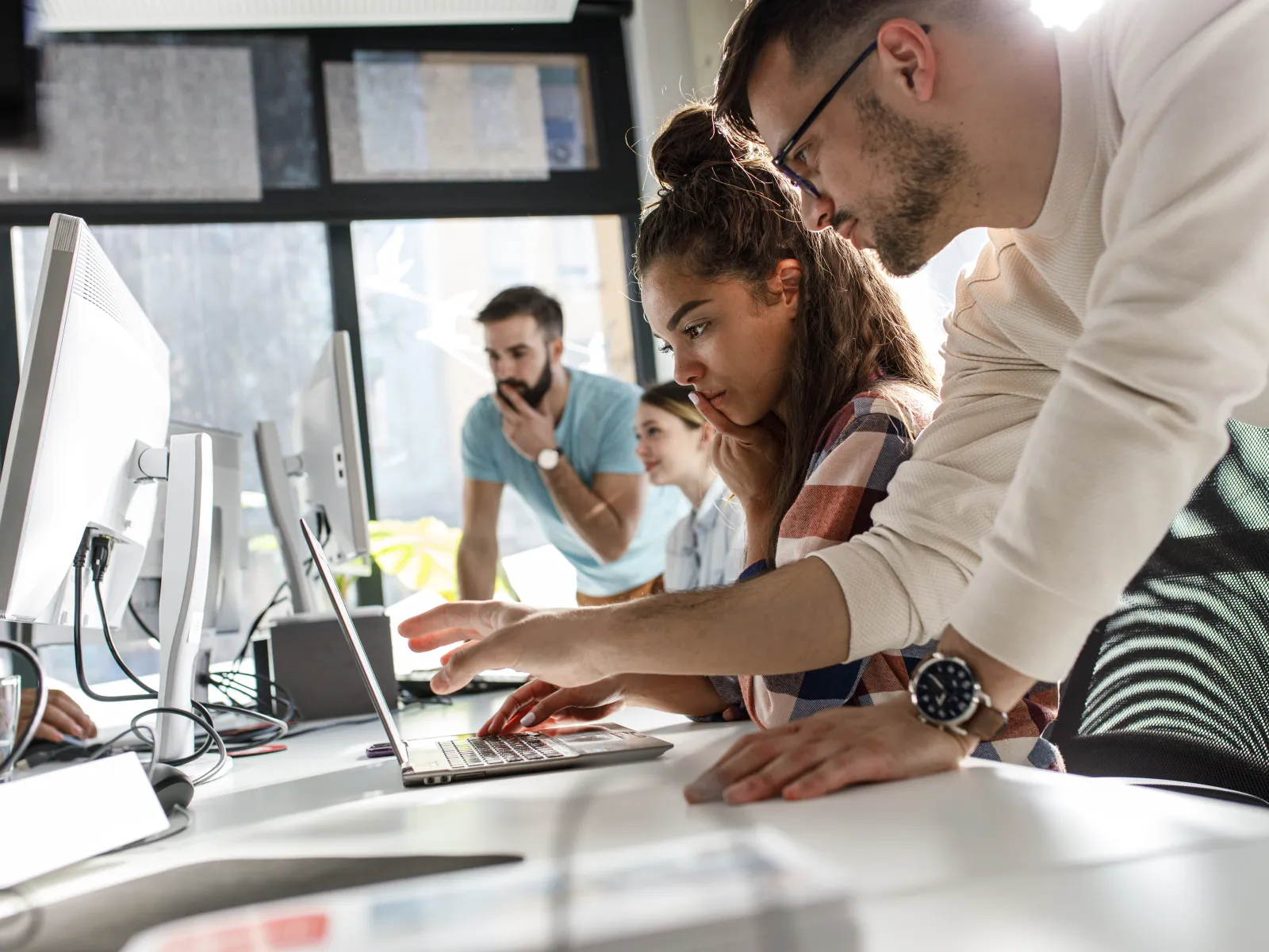 Team of young professionals collaborating at a desk with computers in a modern office space.