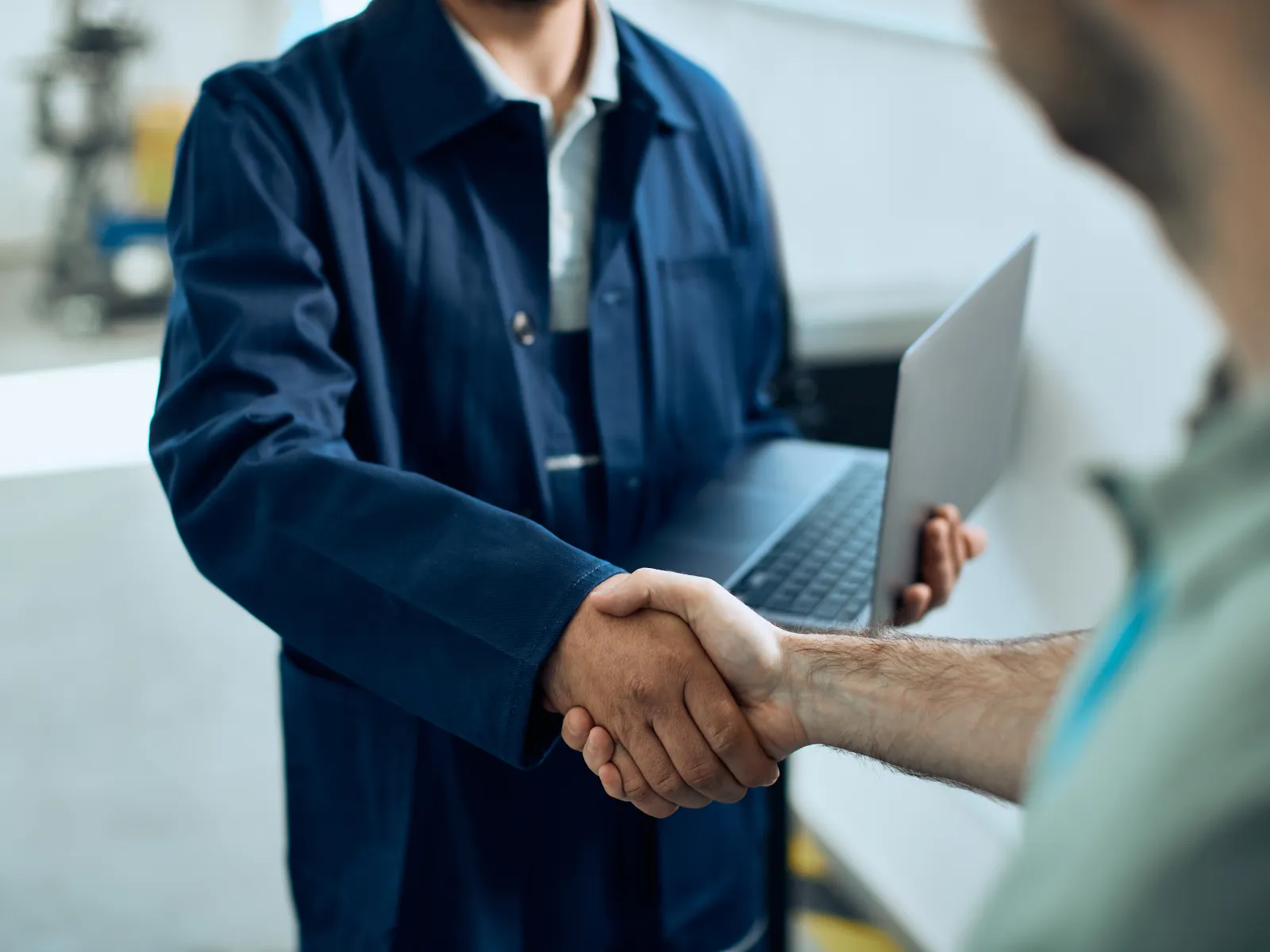 a repair man holding a laptop and shaking a man's hand