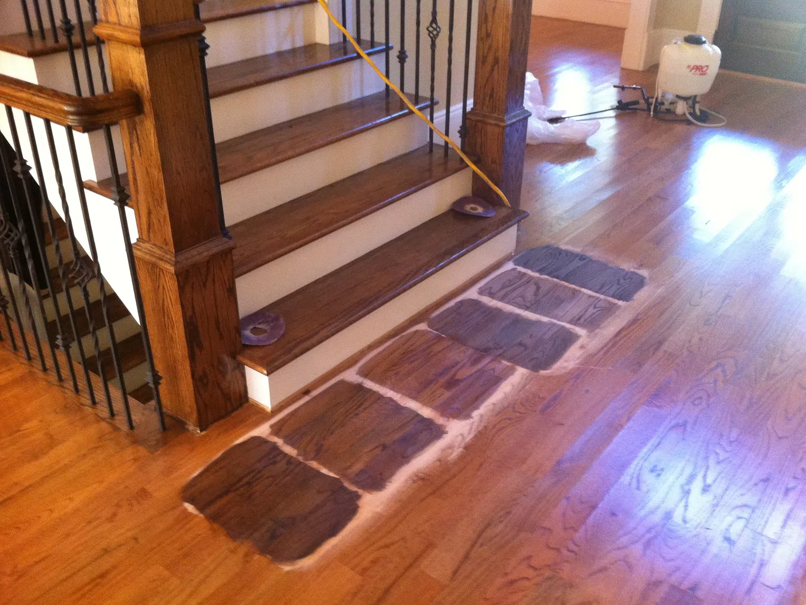 Wood floor repair in progress with wood patches aligned near staircase and sanding equipment nearby