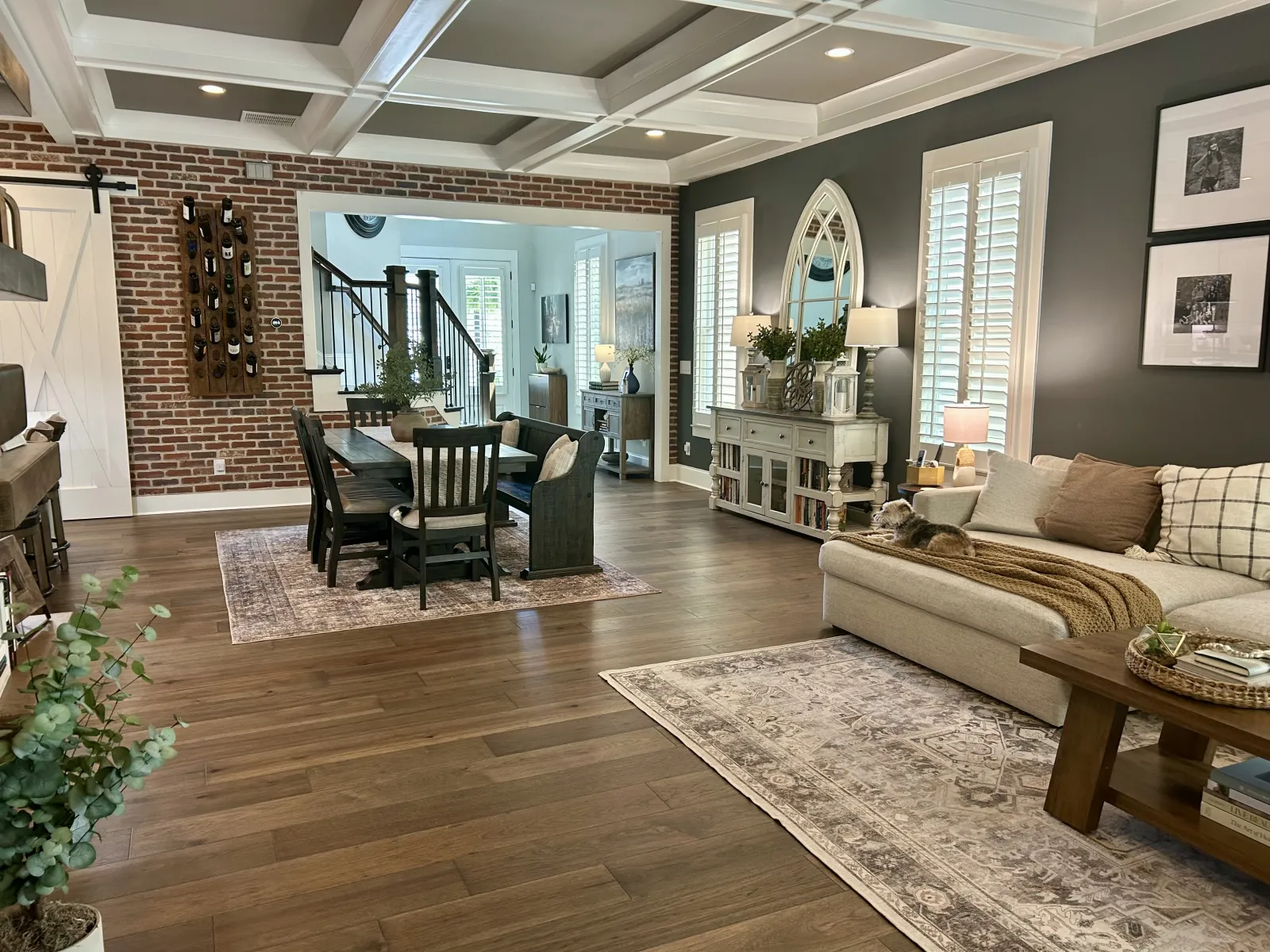 Open living and dining area with wood floors, brick accent wall, neutral furniture, and decorative accents.