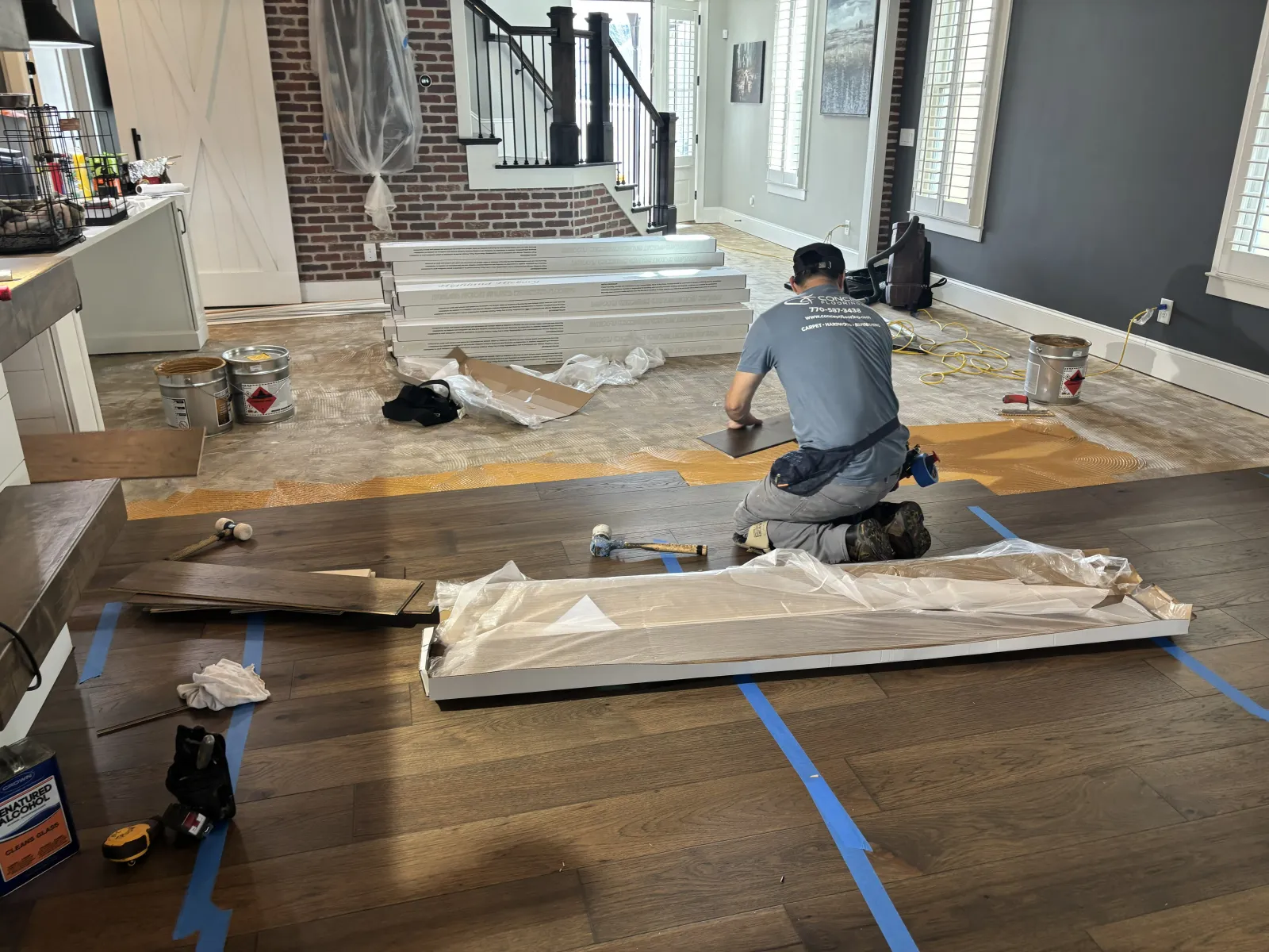 Worker installing dark hardwood flooring in a bright room with tools and materials scattered around.