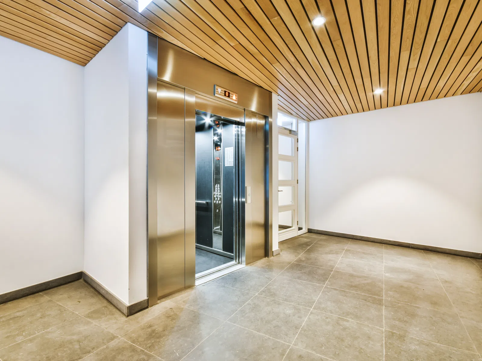 Modern elevator with stainless steel doors in a bright lobby with tiled floor and wooden ceiling