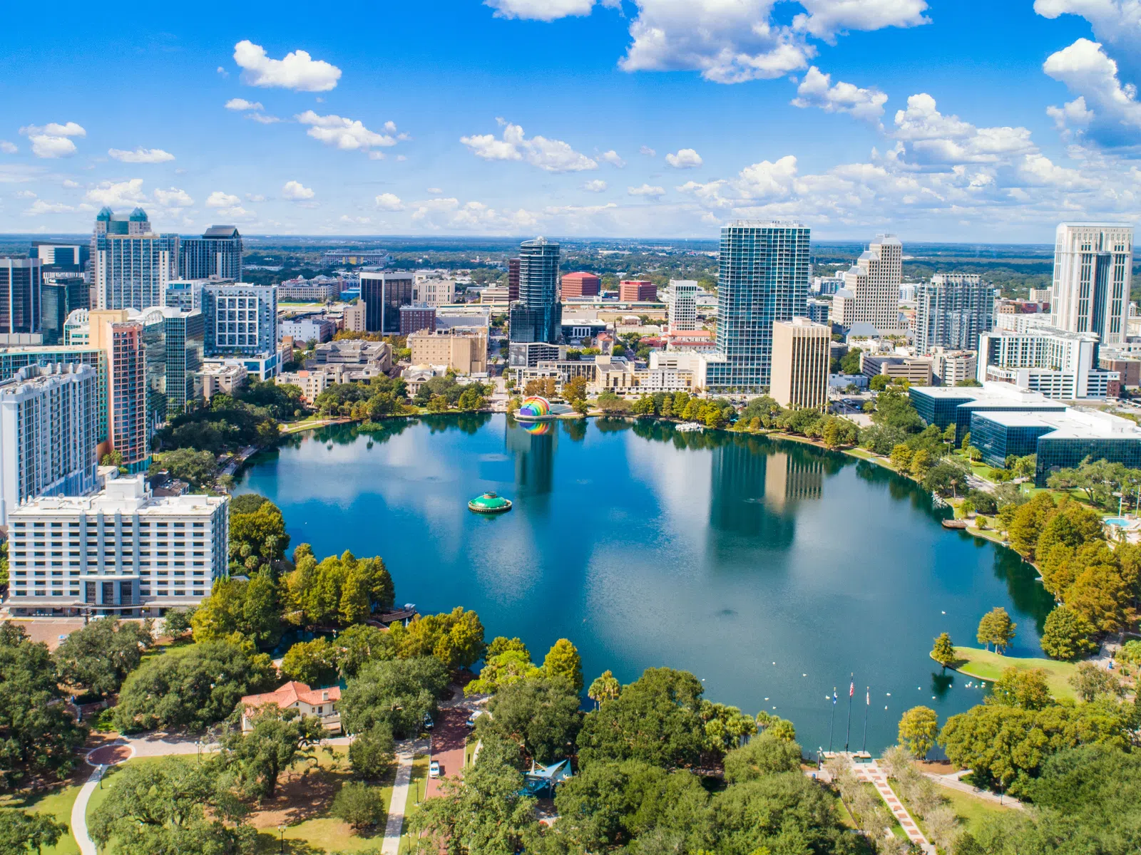 Aerial view of a city skyline with a large central lake surrounded by trees and buildings on a sunny day.