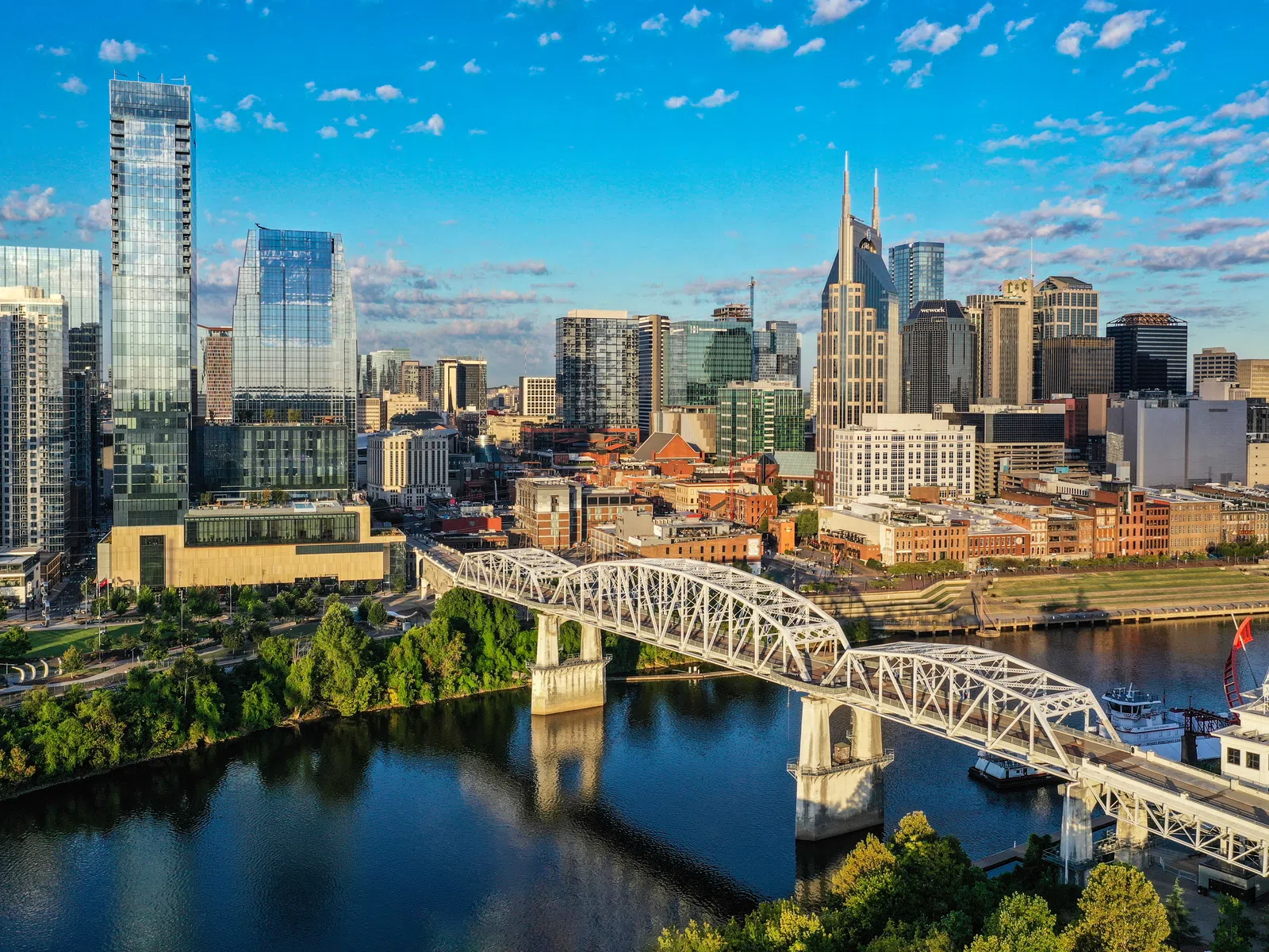 Aerial view of Nashville skyline with river, bridge, and modern high-rise buildings under a blue sky.