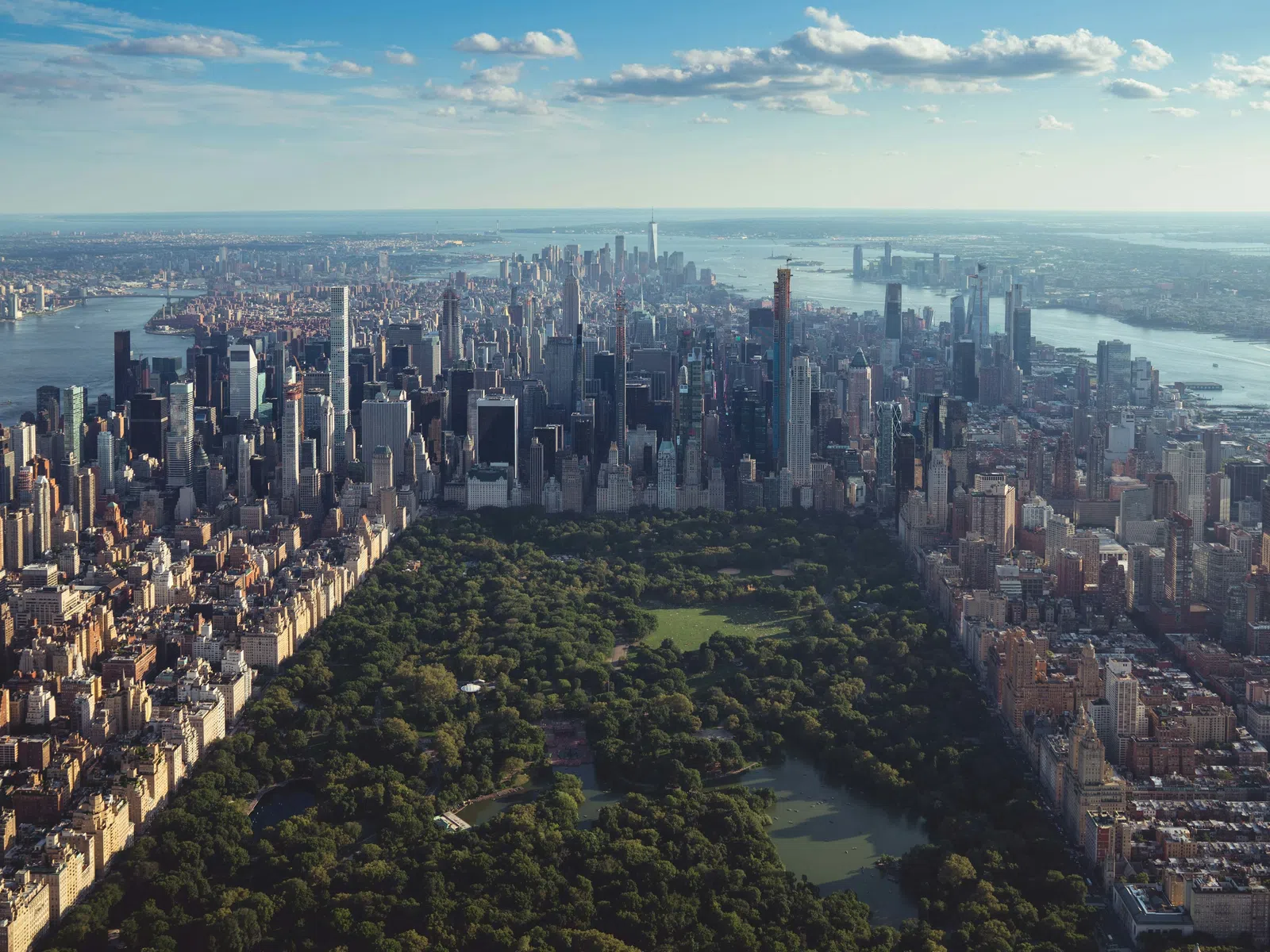 Aerial view of Central Park surrounded by Manhattan skyscrapers under a partly cloudy sky in New York City.