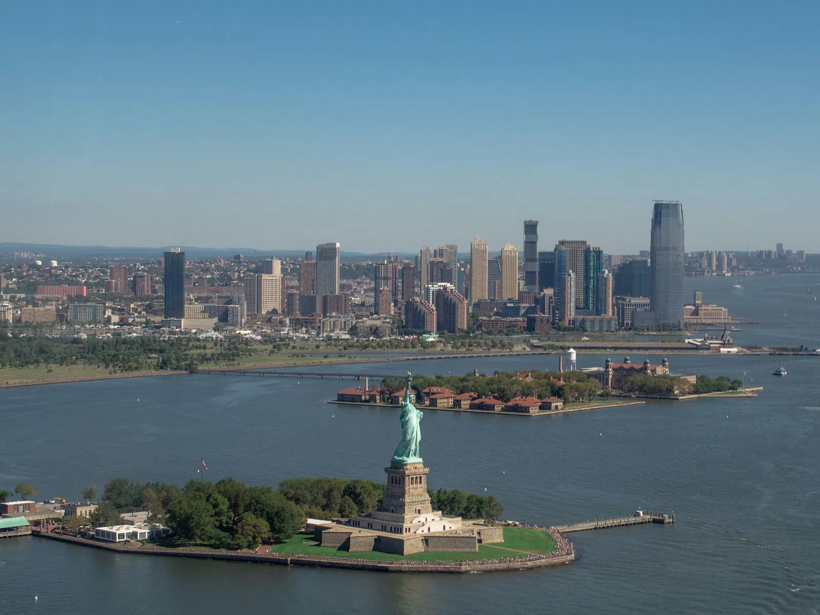 Statue of Liberty on Liberty Island with Manhattan skyline and waterfront in background under clear sky.