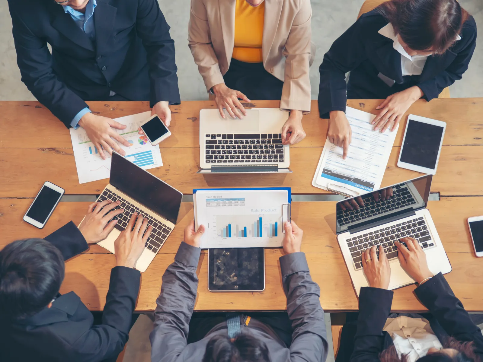 a group of people sitting around a table with laptops and papers
