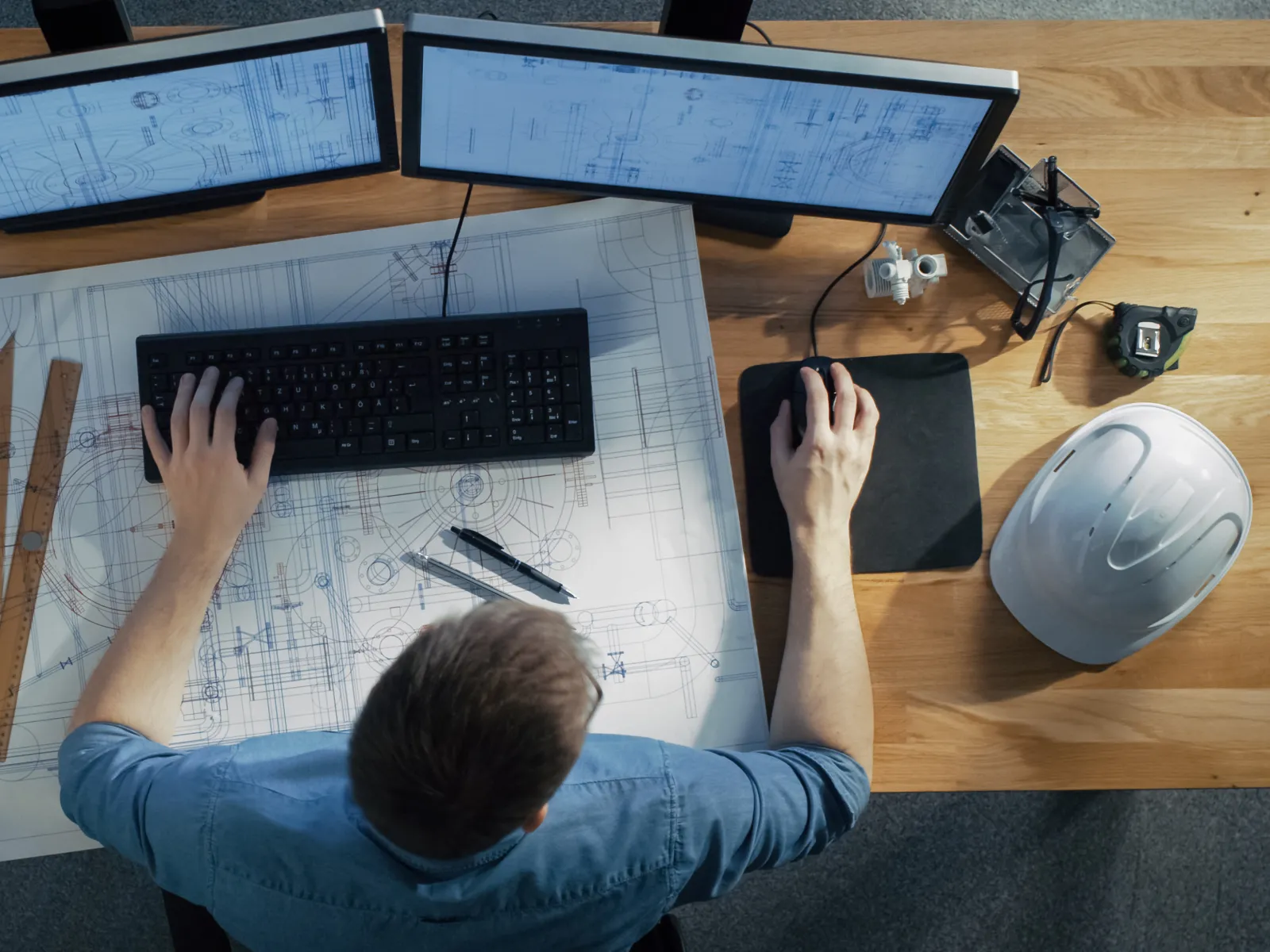 a man sitting at a desk with a computer and a keyboard next to safety gear