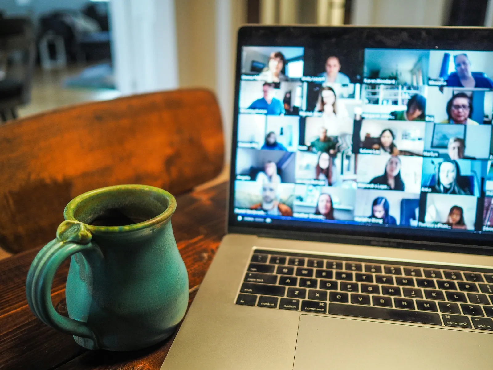 Laptop showing a virtual meeting with multiple participants and a green ceramic coffee mug on a wooden table