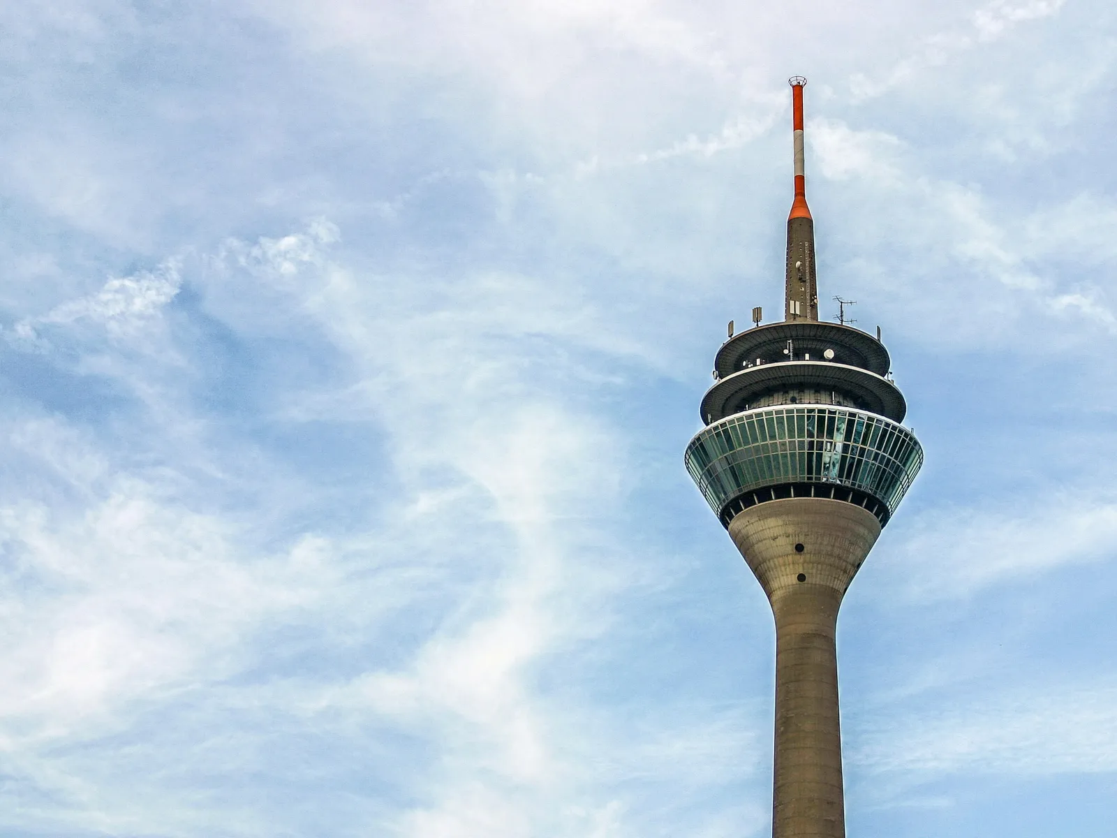 Rhine Tower in Dusseldorf stands tall against a bright blue sky with wispy clouds during daytime.