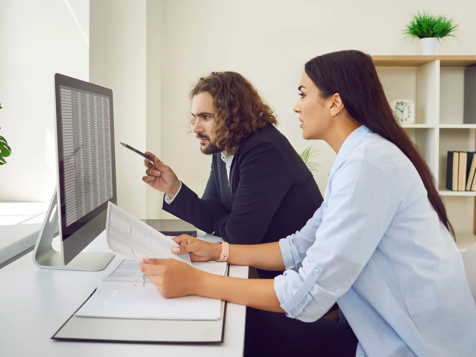Two professionals analyzing data on a computer screen in a modern office environment.