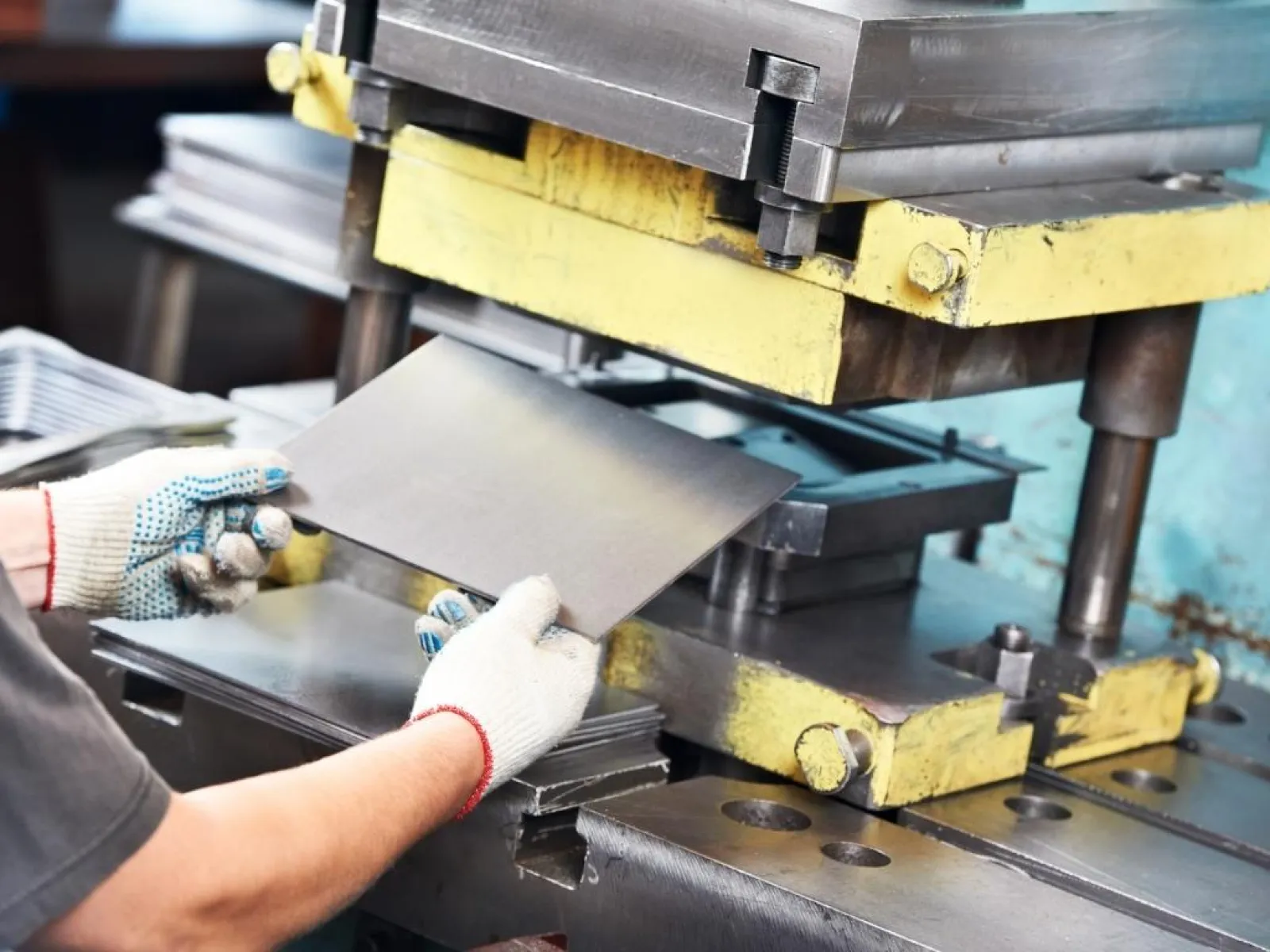Worker in gloves handling metal sheet under heavy industrial press machine in factory setting