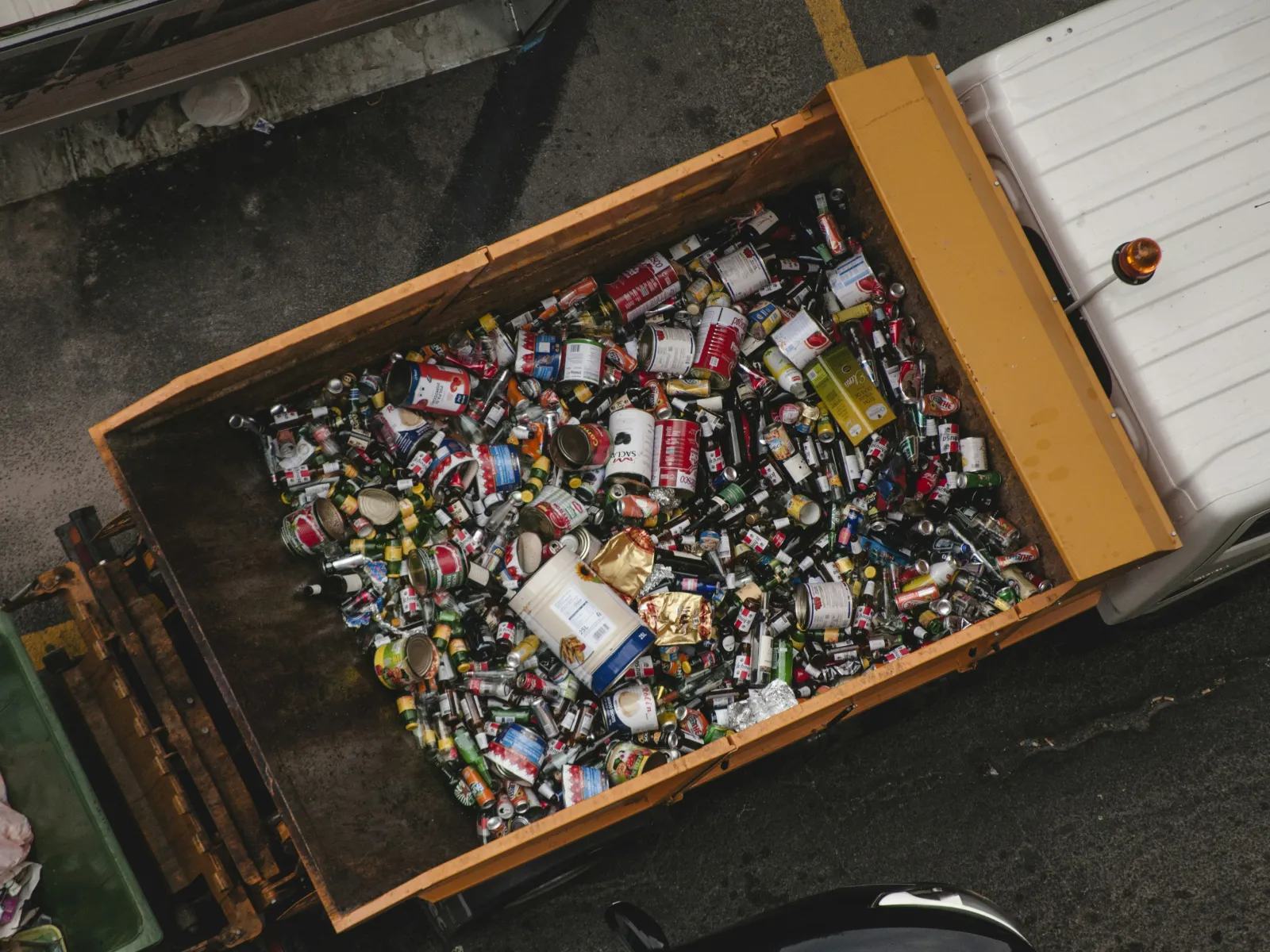 Overhead view of a garbage truck filled with assorted cans and plastic bottles for recycling on a street.