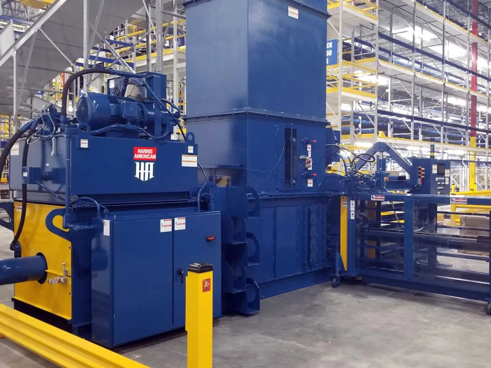 Large blue industrial machine in a warehouse with metal racks and concrete floor surrounding it