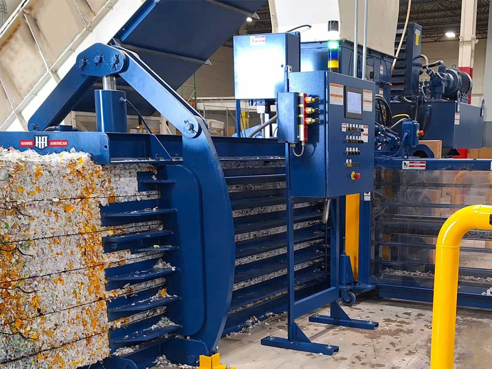 Industrial blue baler machine compressing large bales of recyclable paper inside a factory.