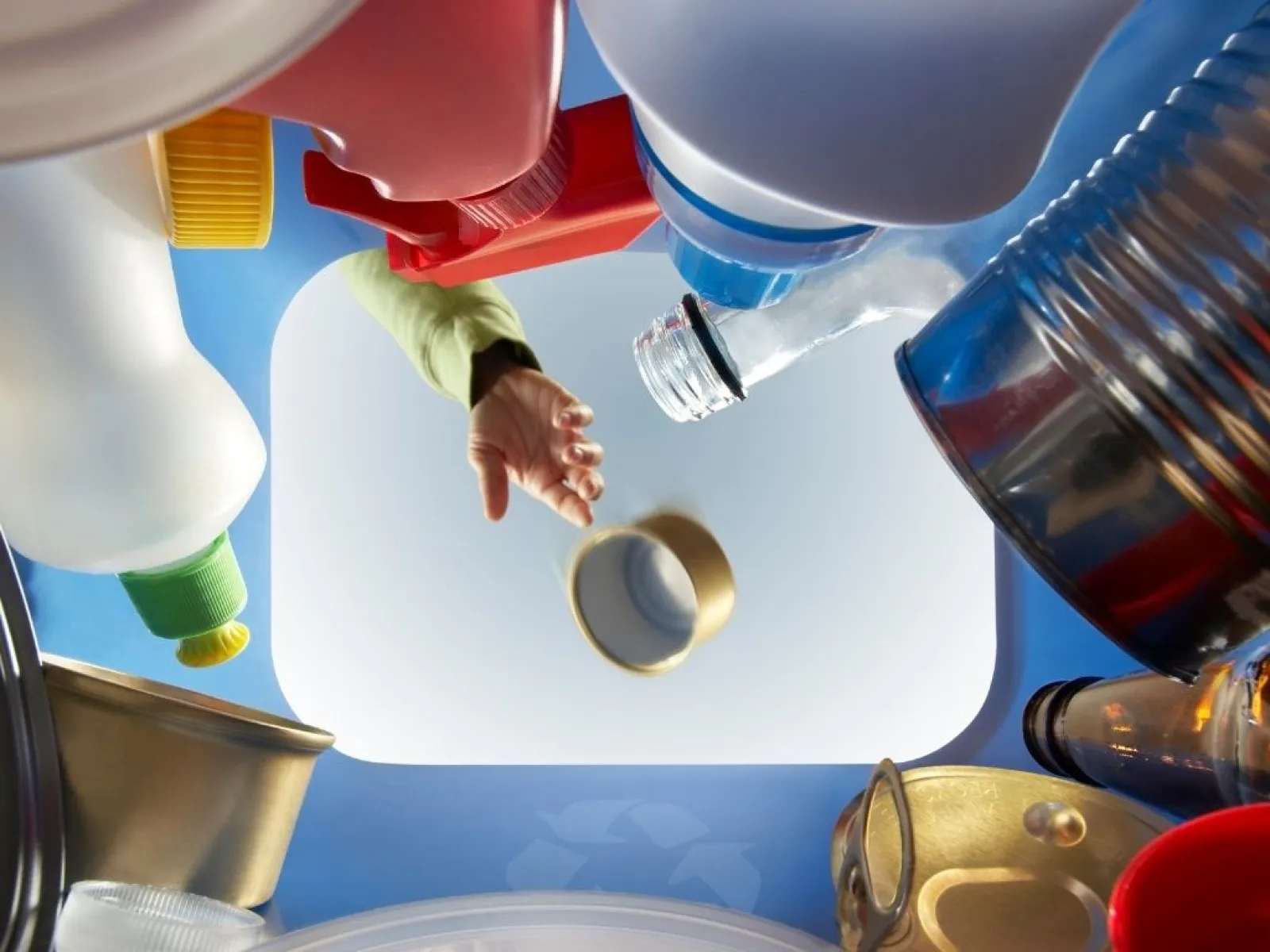 Person throwing recyclable items like bottles and cans into a recycling bin from inside view