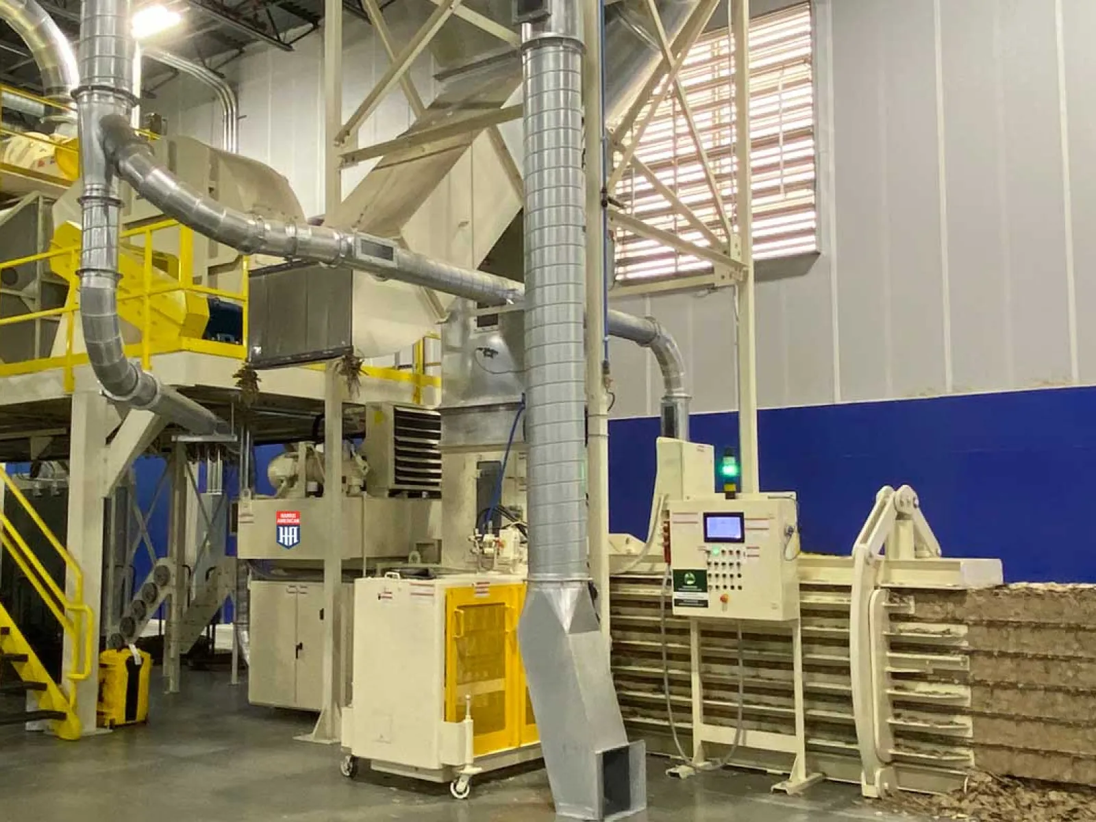 Industrial green baler machine compressing cardboard bales inside a warehouse.