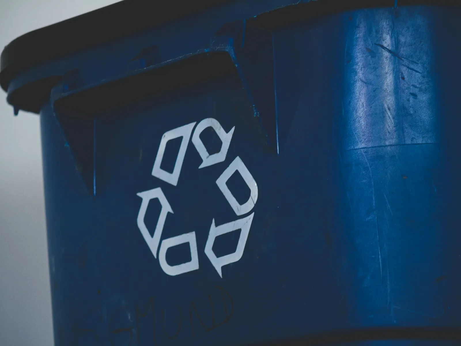 Close-up of a blue recycling bin with a white recycling symbol on the front against a blurred background