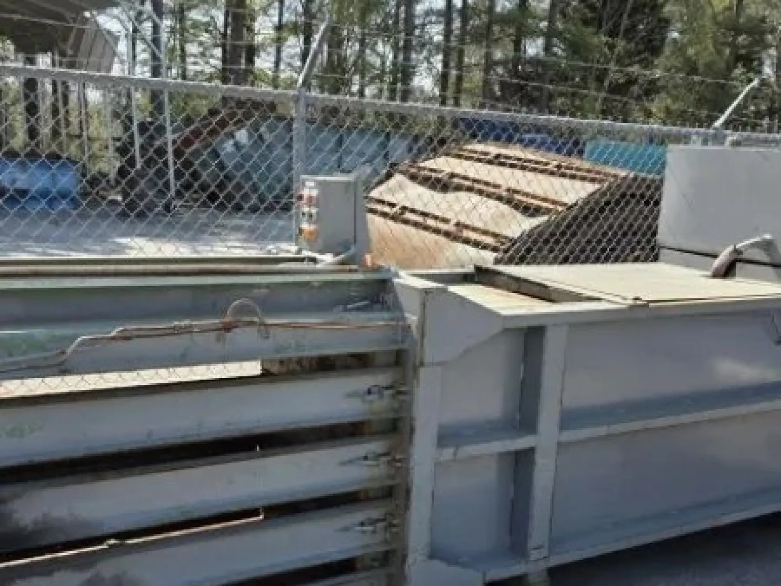 Large industrial metal baler machine used for compacting materials outdoors by a chain link fence