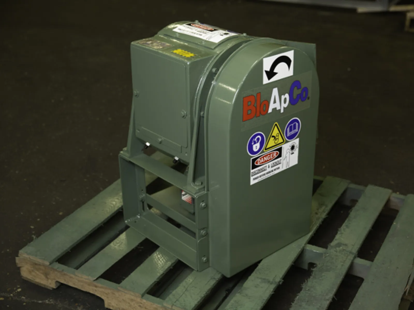 BloApCo industrial machine with safety warning labels on a wooden pallet in a workshop setting.