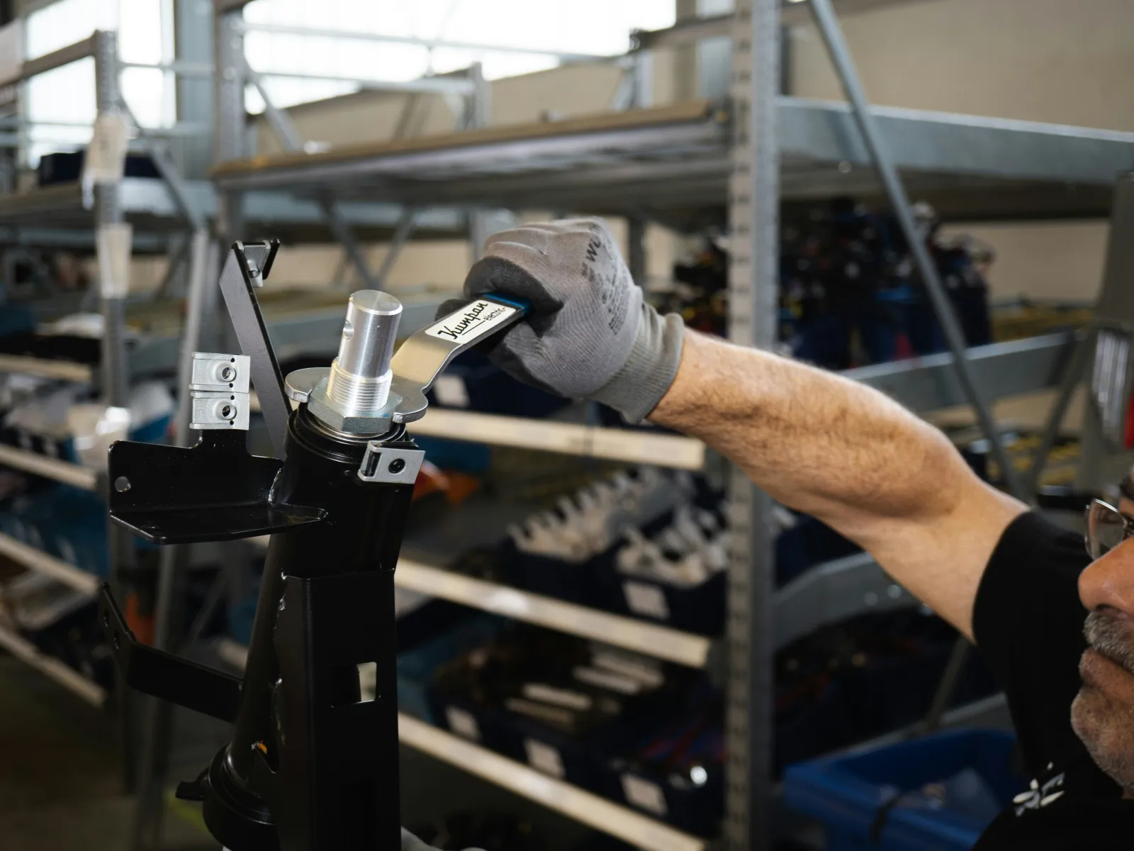 Mechanic using a wrench to tighten a metallic component on a black mechanical assembly in a workshop.