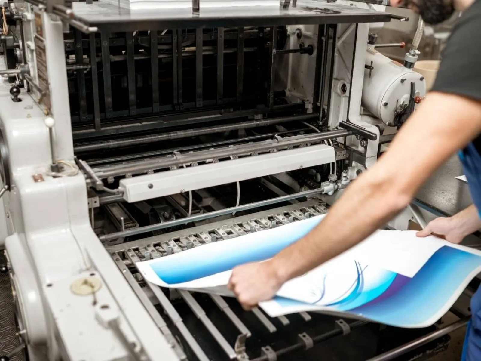 Man inspecting freshly printed material coming out of an industrial printing press in a factory setting
