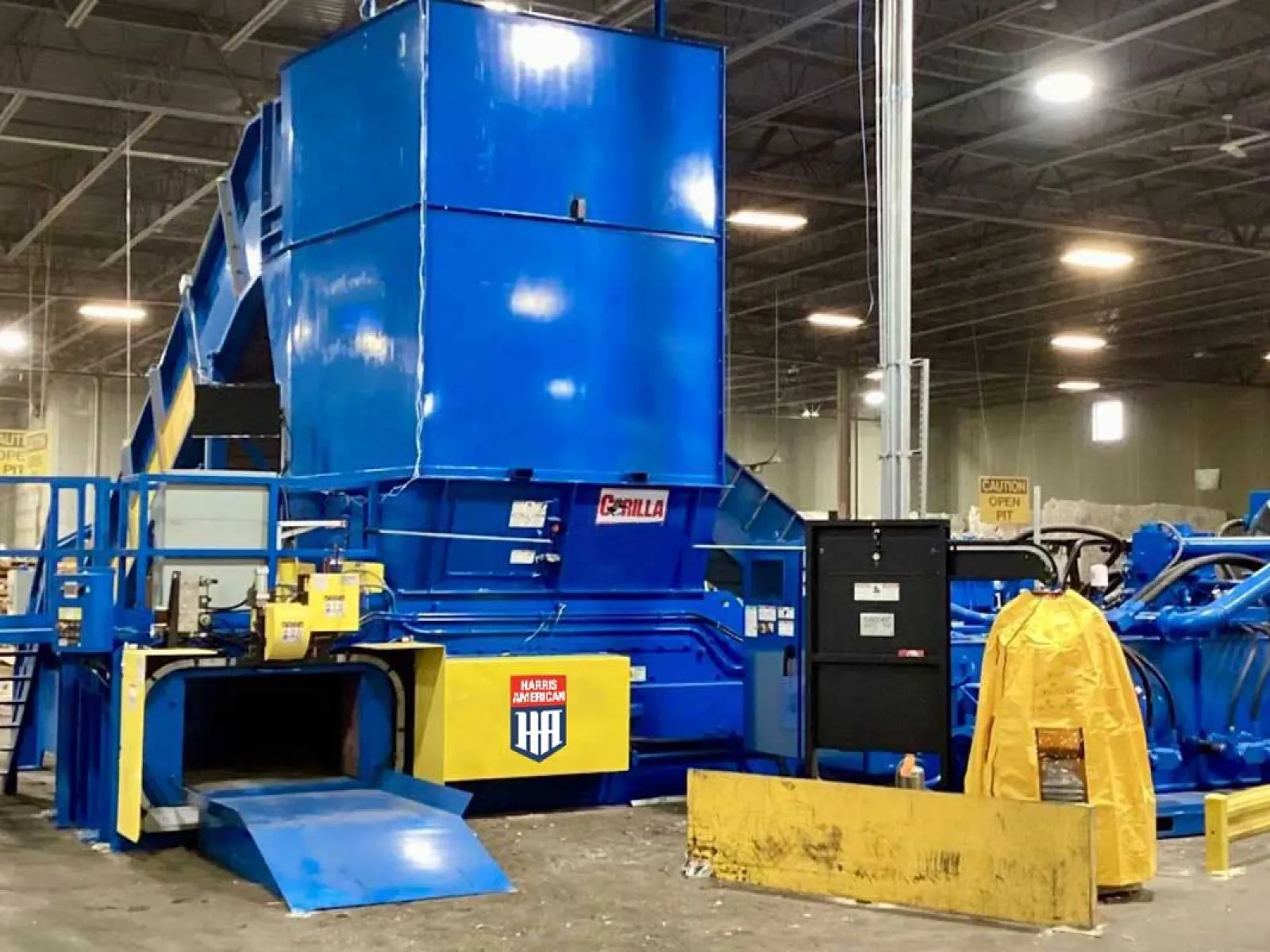 Large blue industrial machine in warehouse used for heavy material processing with safety barriers and ramps.