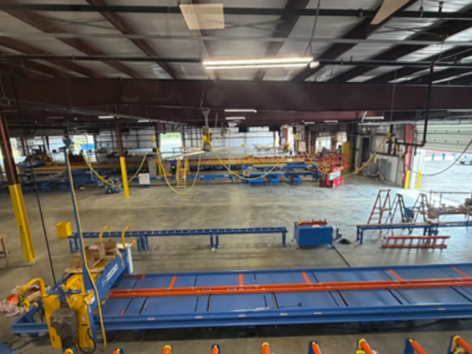 Spacious industrial warehouse with metal beams, large machinery, and conveyor systems under bright lighting.