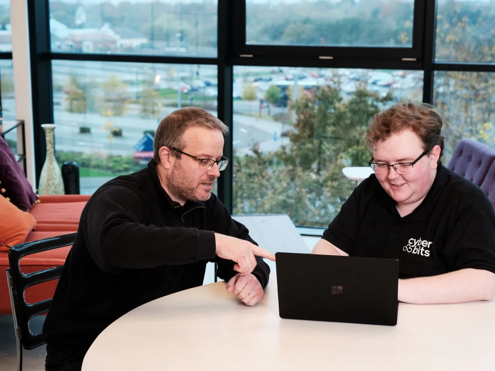a couple of men sitting at a table looking at a laptop