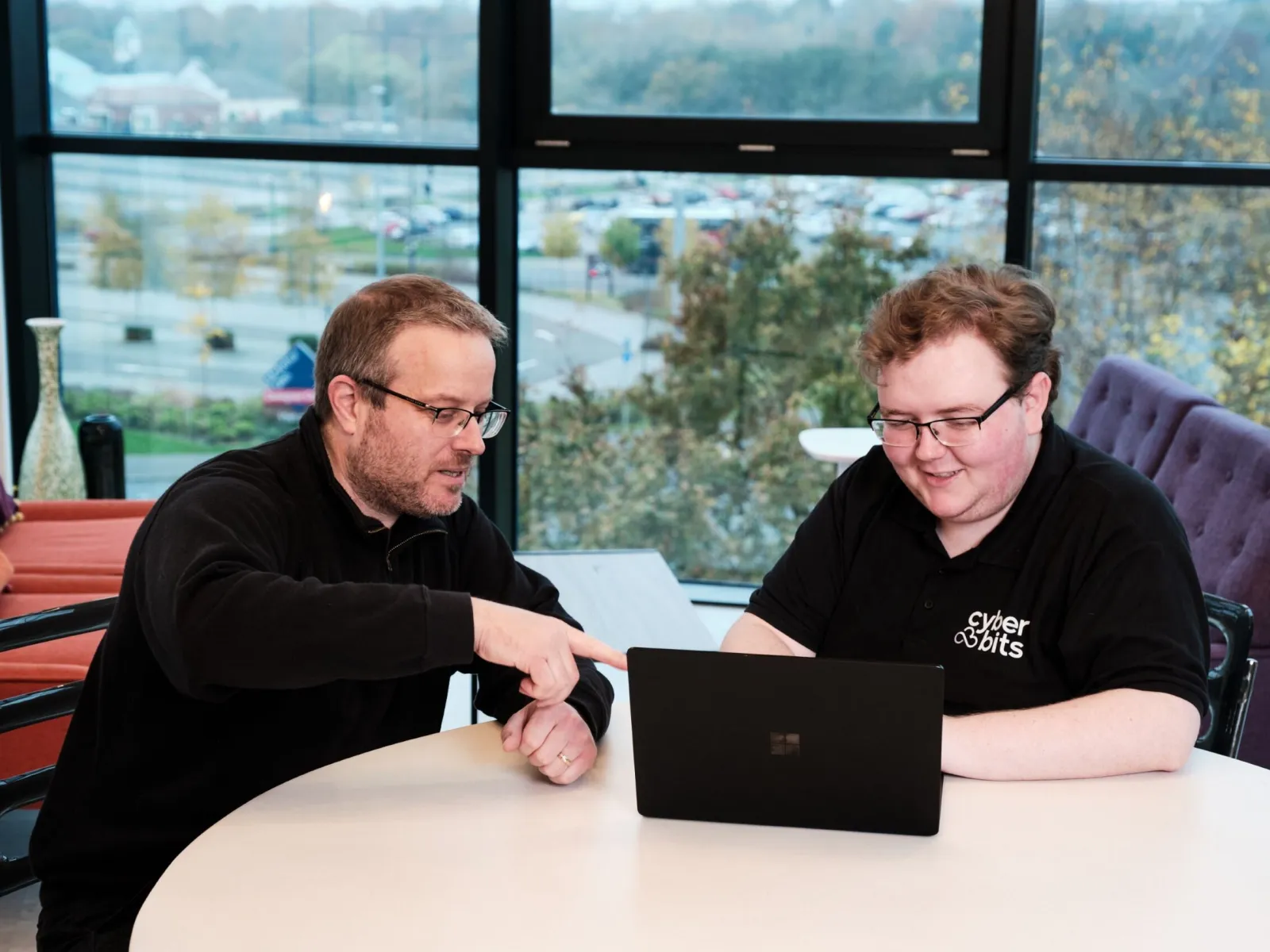 a couple of men sitting at a table looking at a laptop