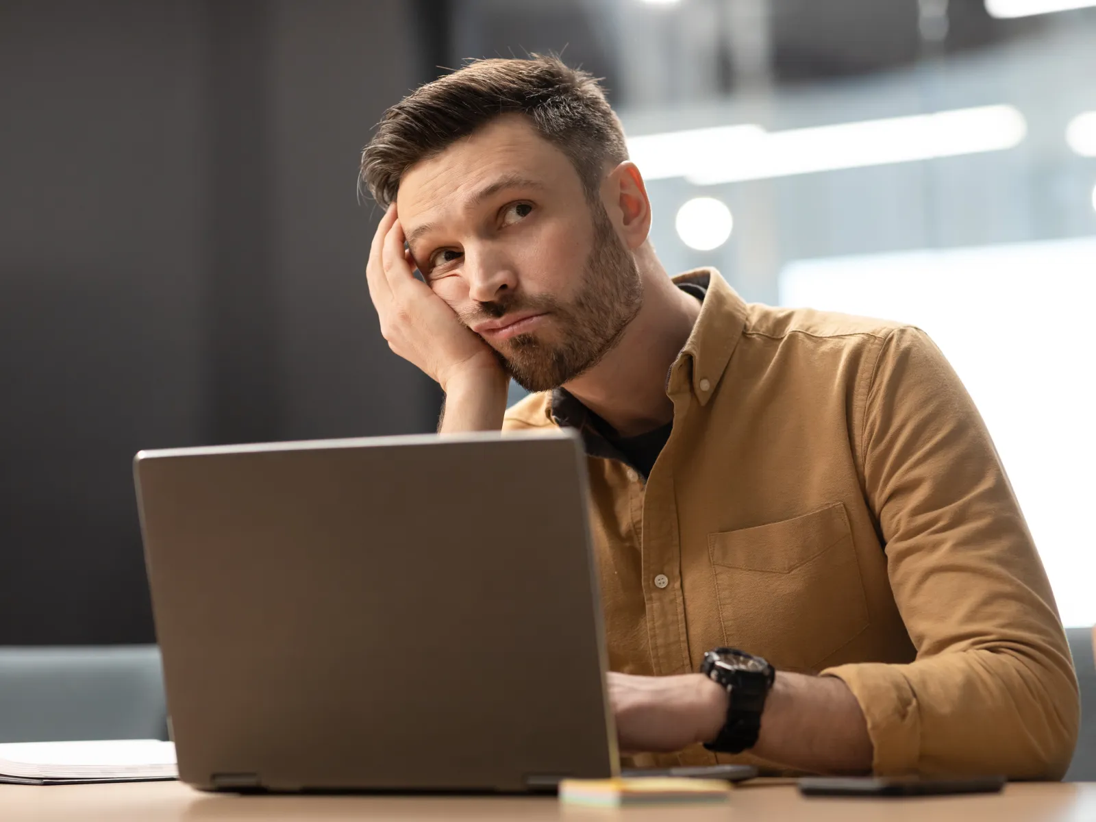 a man with his hand on his face looking at a laptop