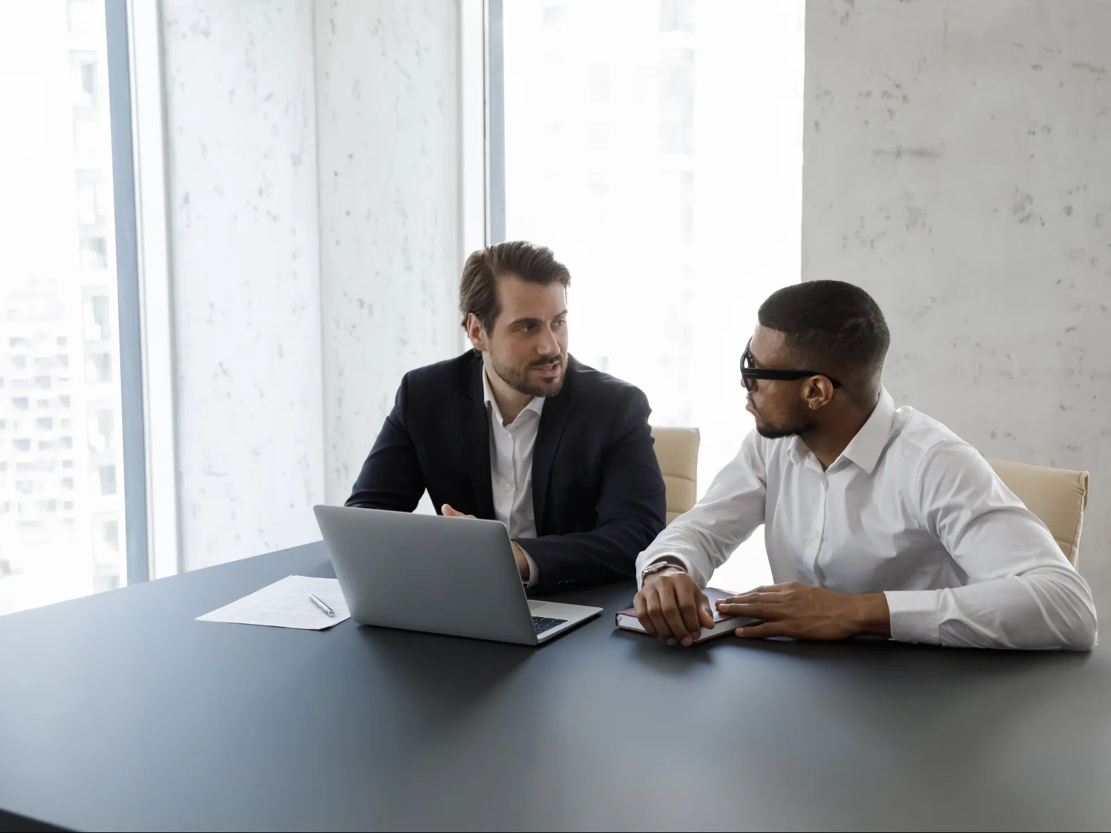 men sitting at a table looking at a laptop