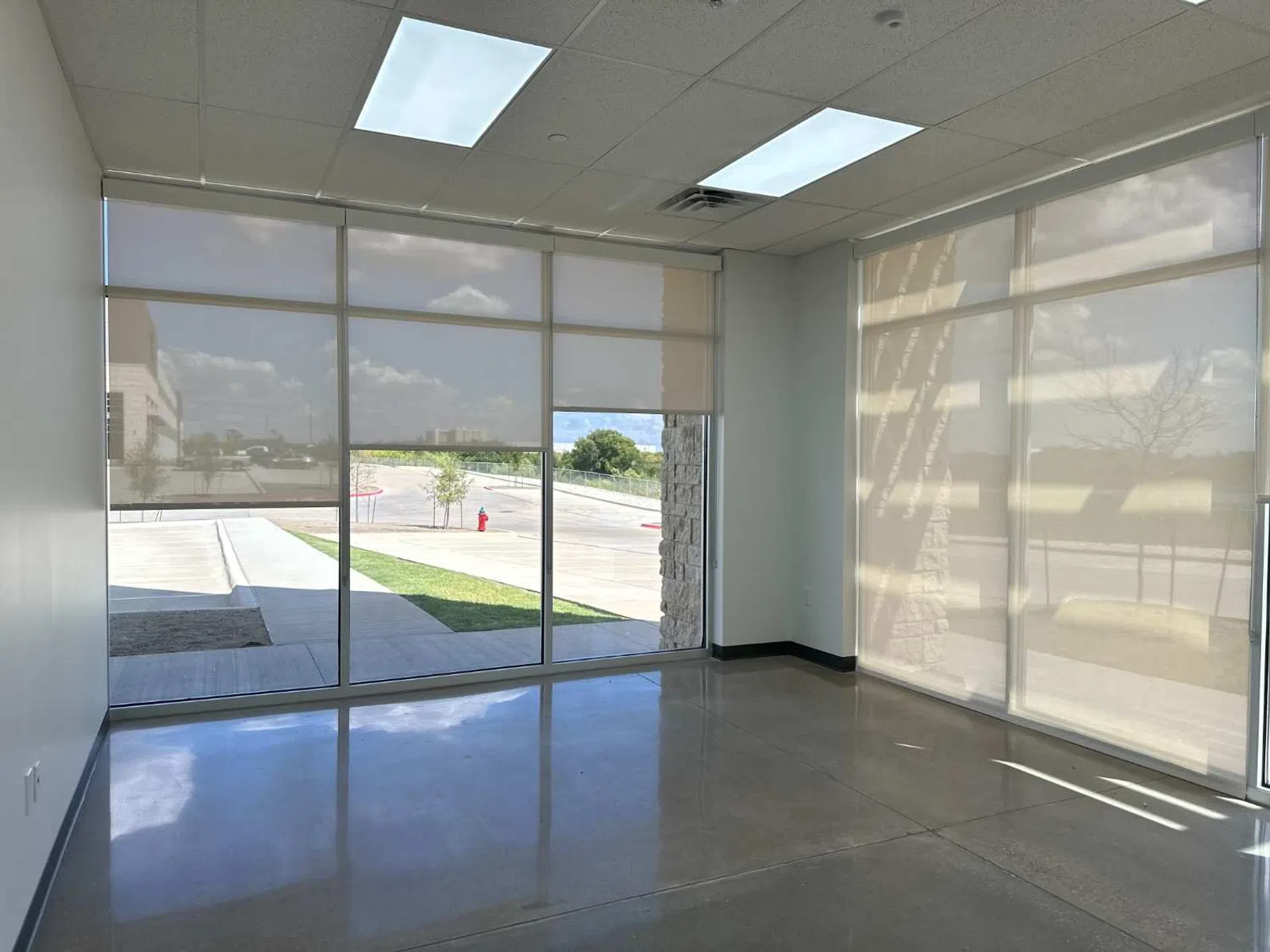 Empty room with large windows covered by roller shades letting in soft natural light and polished concrete floor