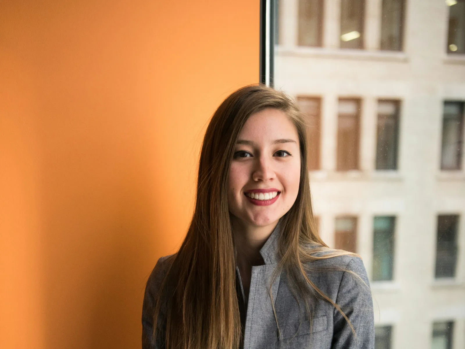 Man smiling and gesturing while video calling on laptop in a sunlit office with an open magazine on the desk.