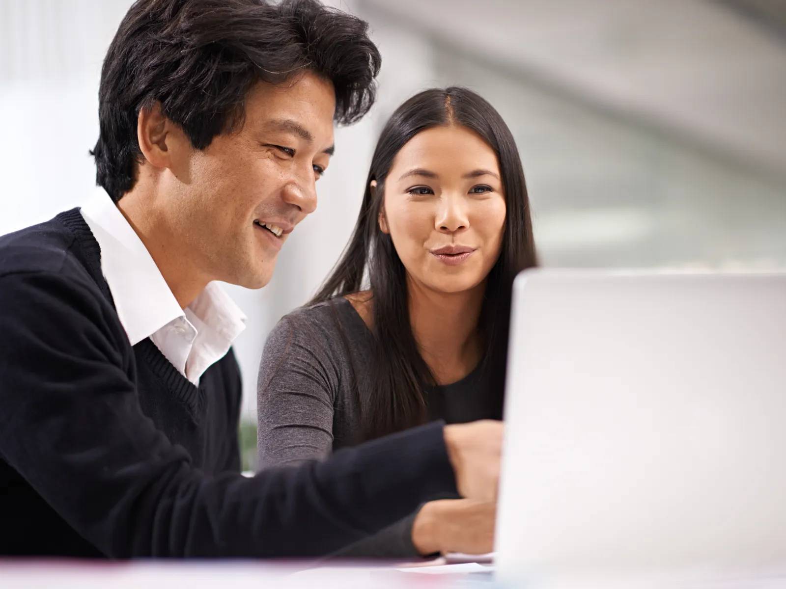 Two colleagues collaborating and smiling while working on a laptop in a modern office environment