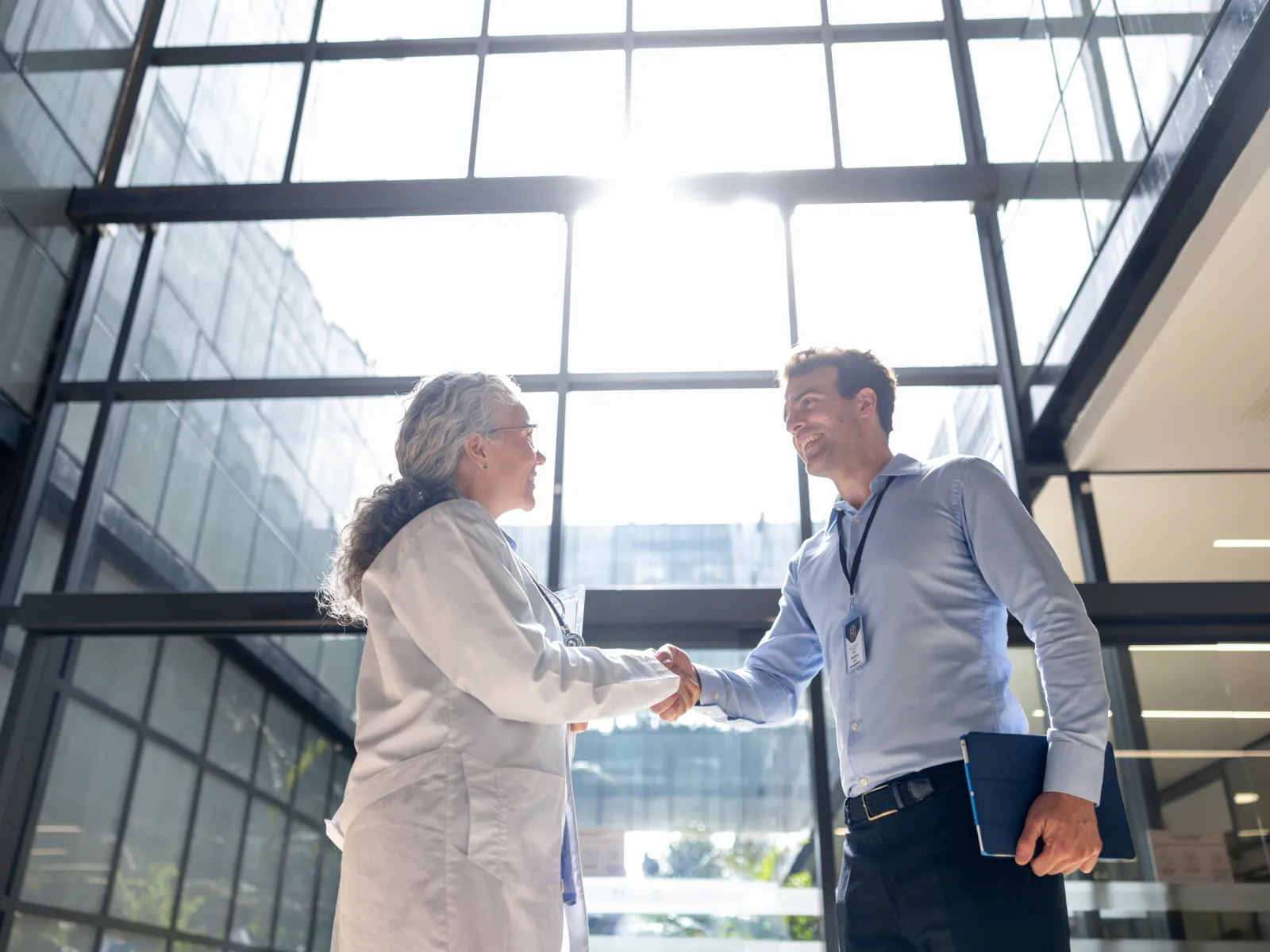 Two business professionals shaking hands in a modern office with large windows and natural light.