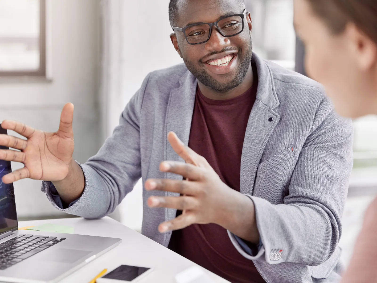 Smiling businessman explains financial charts on laptop during meeting in bright modern office.