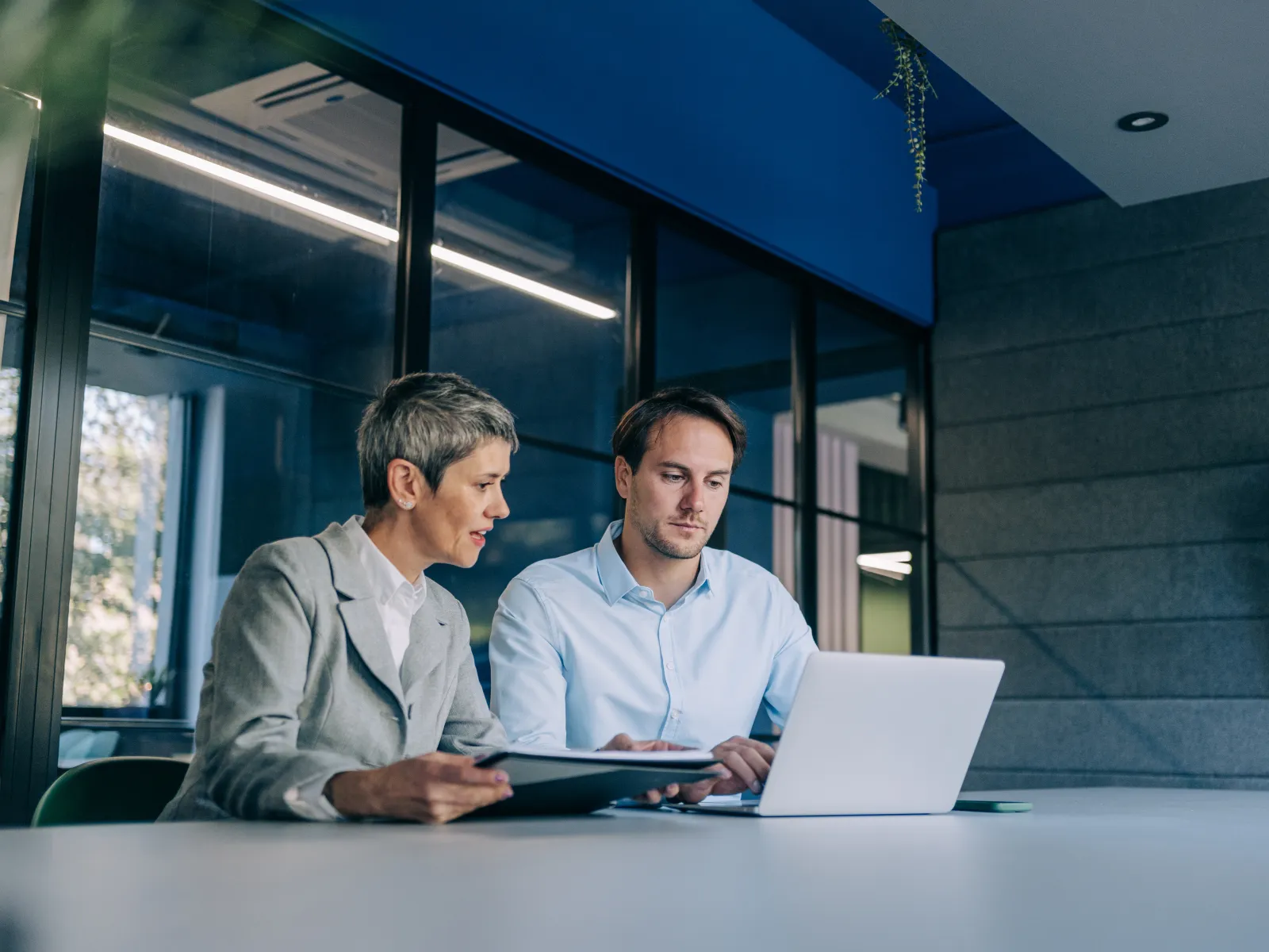 Two professionals collaborating on a project in a modern office, reviewing information on laptop and tablet.