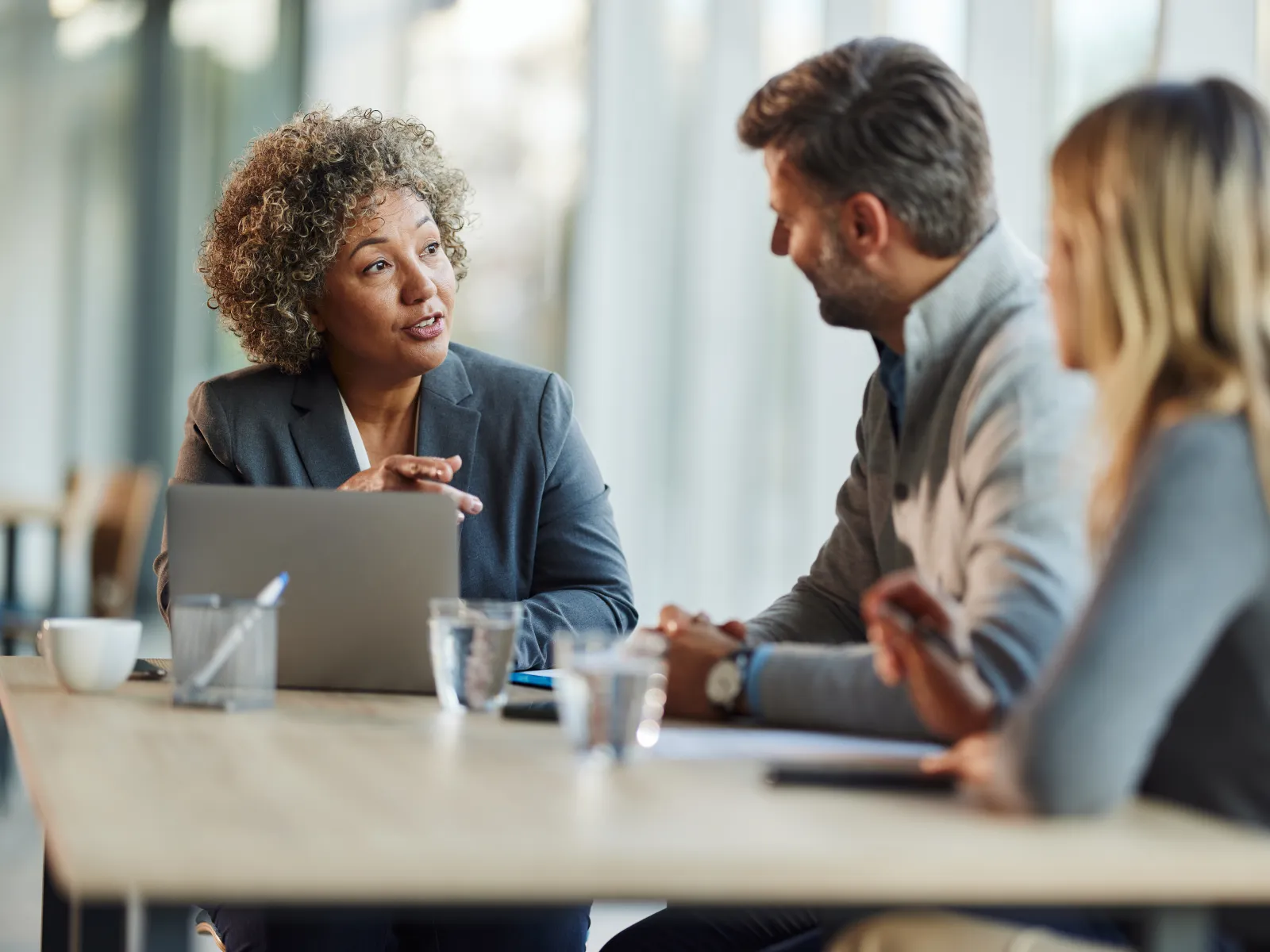 Three professionals engaged in a business meeting discussing ideas around a table with a laptop and documents.
