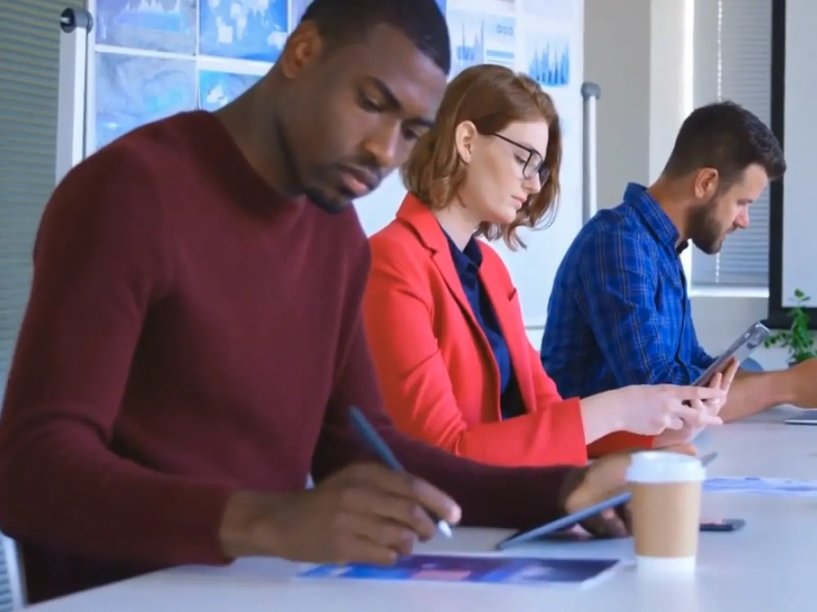 Diverse professionals focused on digital devices and paperwork during office meeting with data charts in background