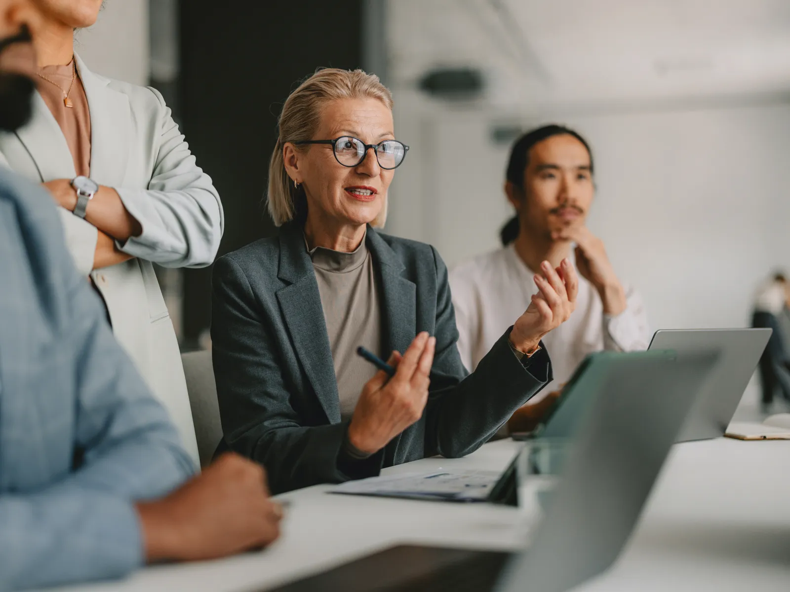 Businesswoman leading discussion in modern office with diverse team and laptops