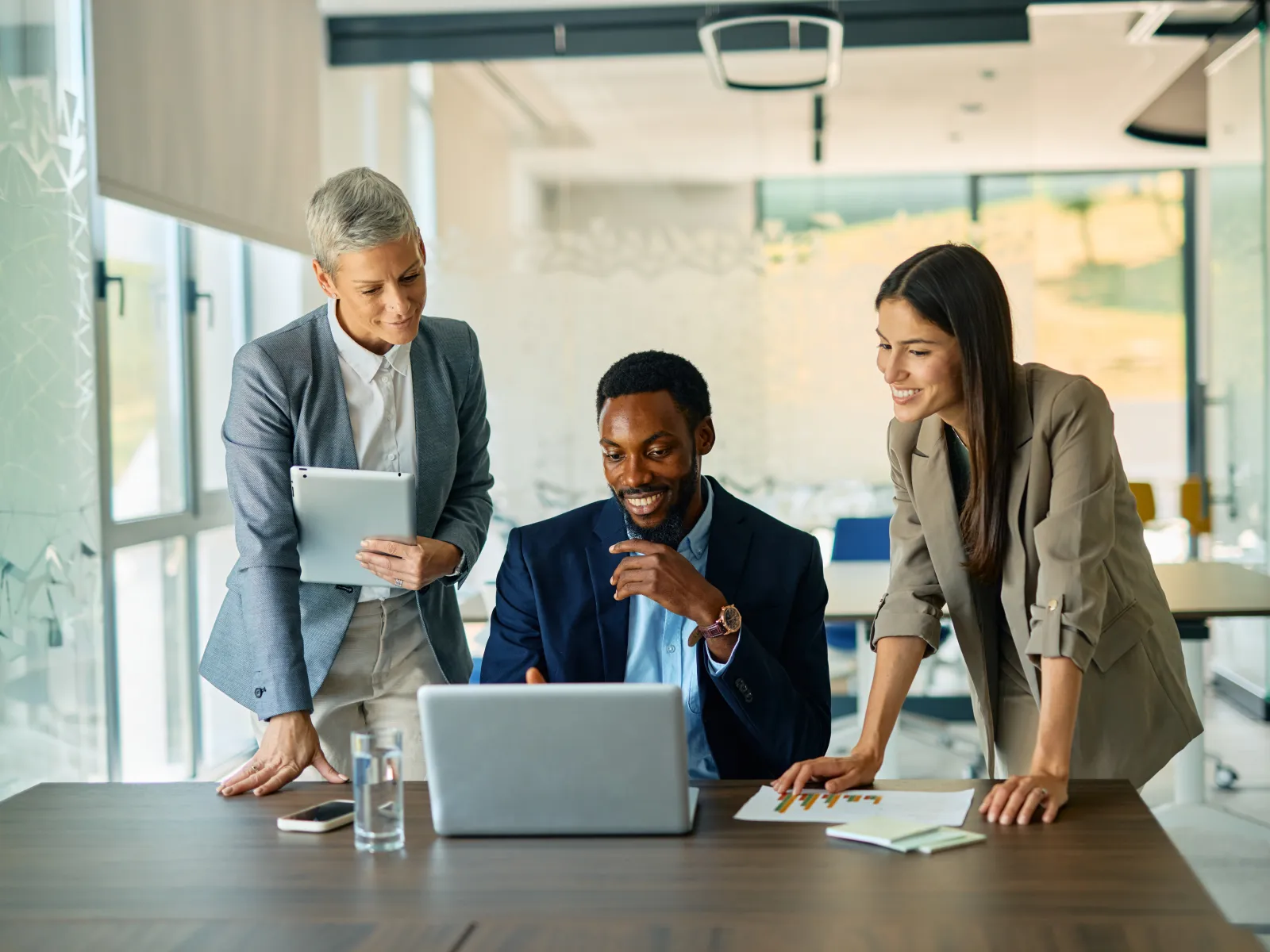 Three diverse business colleagues collaborating on a project using a laptop in a modern office.