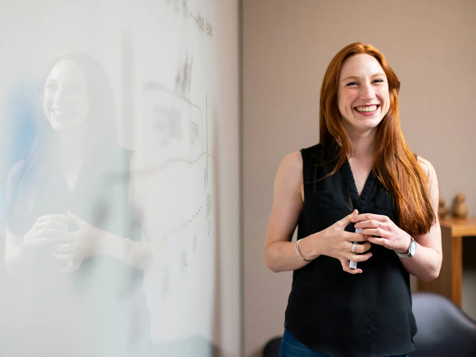 Smiling redhead woman standing by a whiteboard with notes, reflecting confidence and positivity in a modern office.