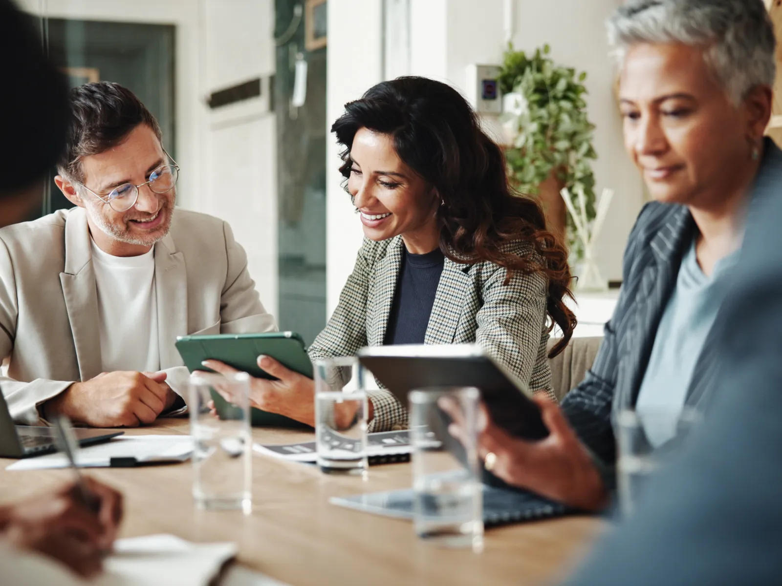 Diverse business team collaborating around a table using tablets and laptops in a modern office setting.