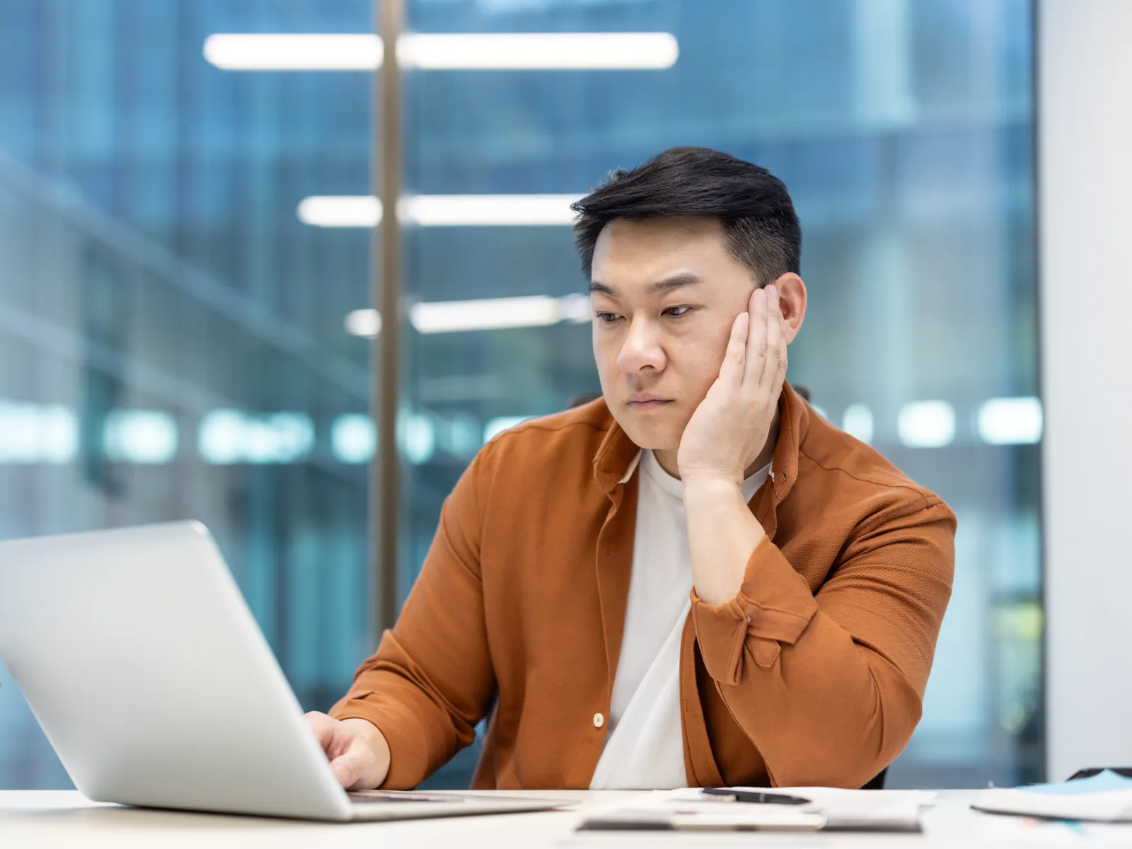 White dome security camera mounted on wall inside modern glass building with blue sky reflection.
